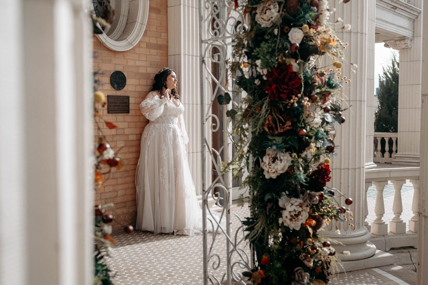 A white wedding dress silhouette against a brick wall adorned with floral decorations.