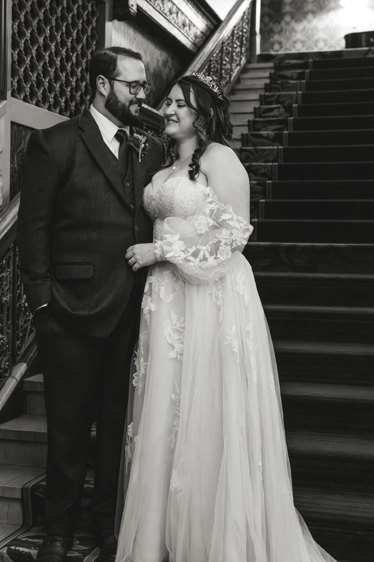 Black and white photo of a bride and groom sharing a romantic moment on an elegant staircase.