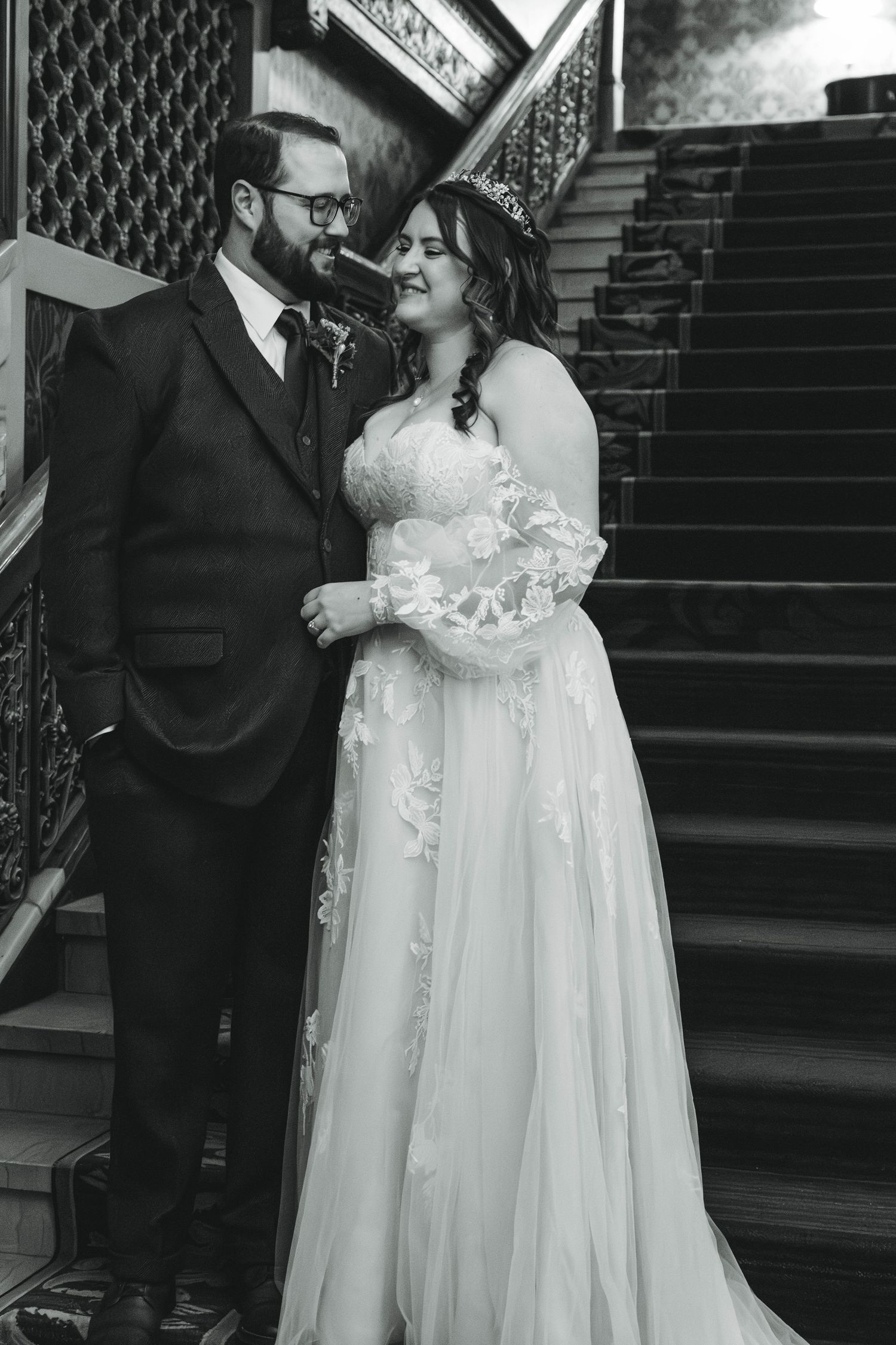 A black and white wedding photo of a couple sharing an intimate moment on an elegant staircase.