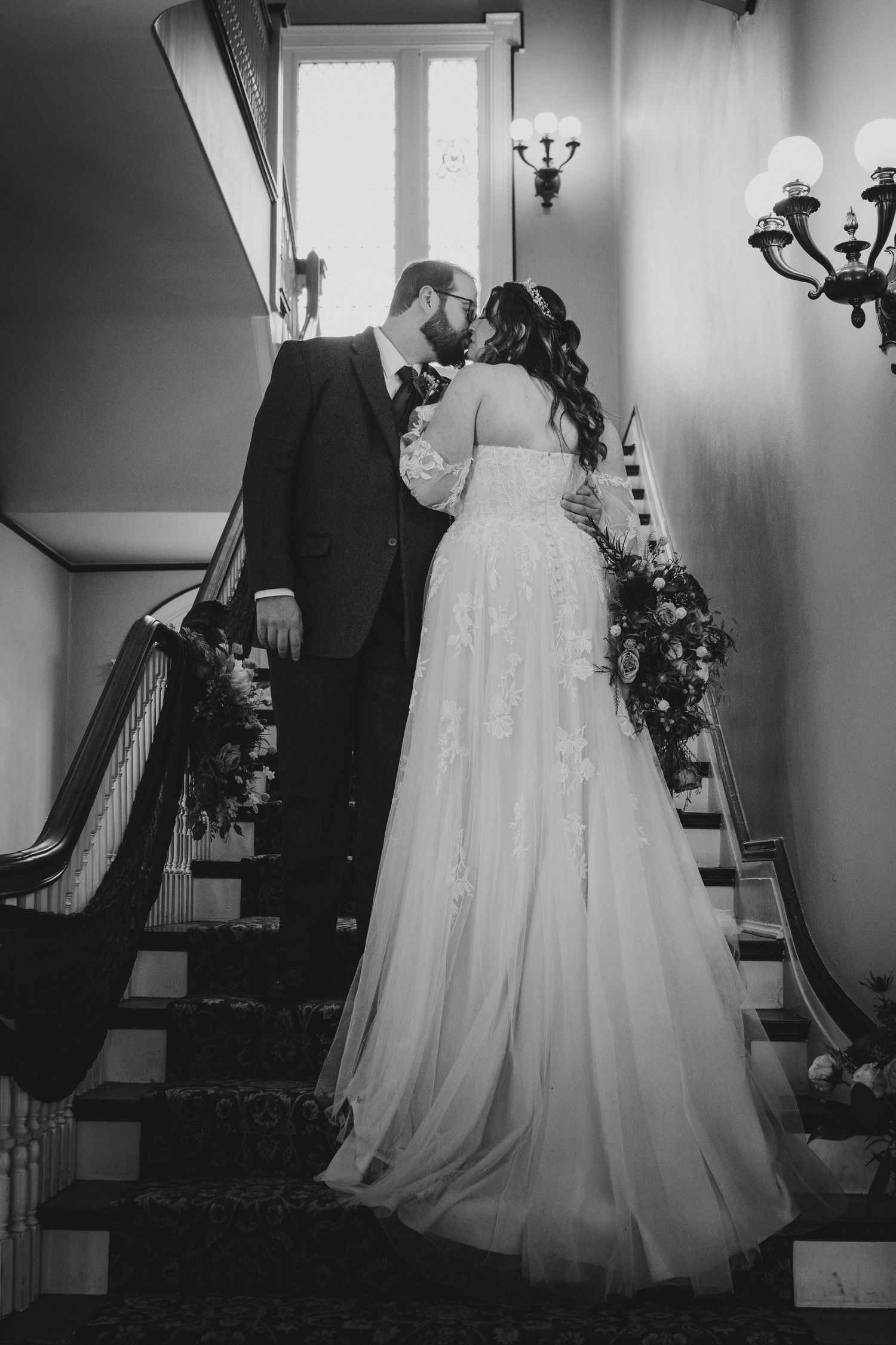 A romantic black and white photo of newlyweds on an elegant staircase with floral decorations.
