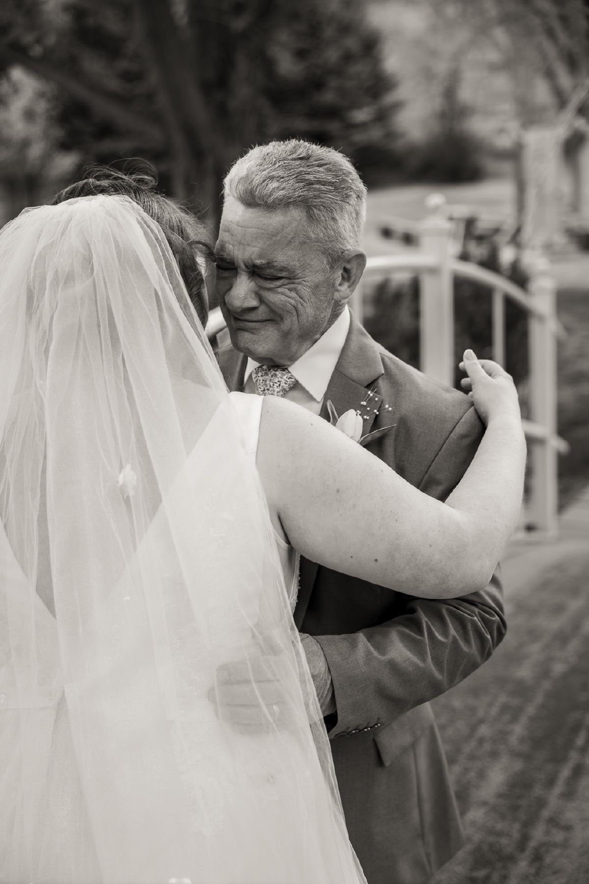 Emotional black and white photo of a father crying while embracing his bride daughter on her wedding day.