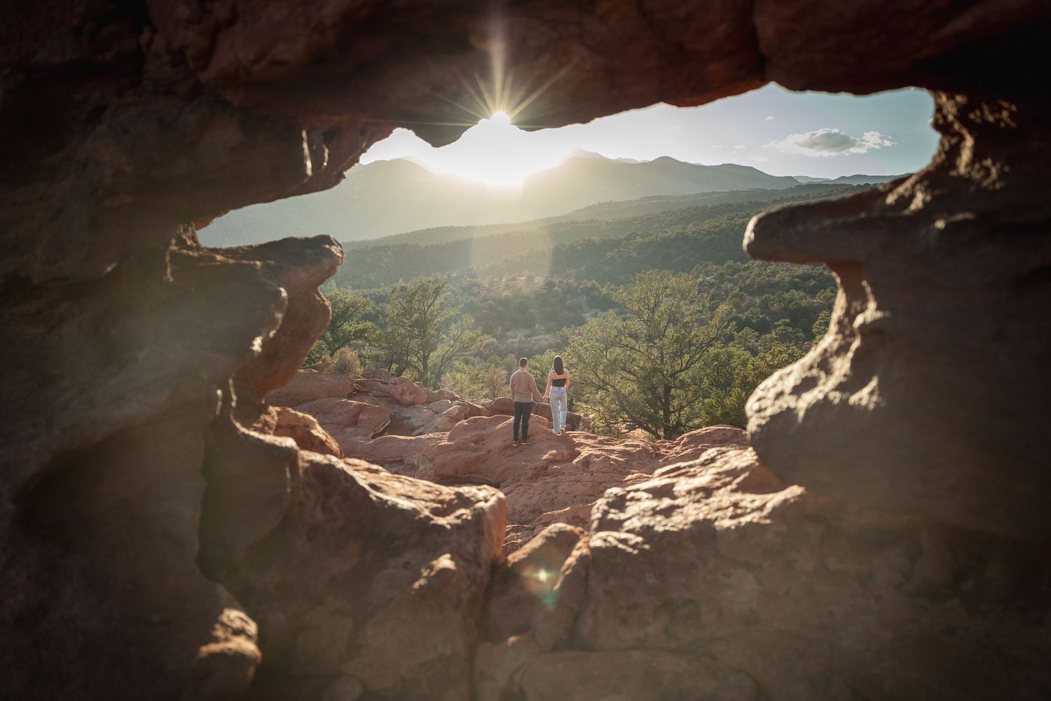 Natural stone arch frames scenic mountain vista with sunburst.