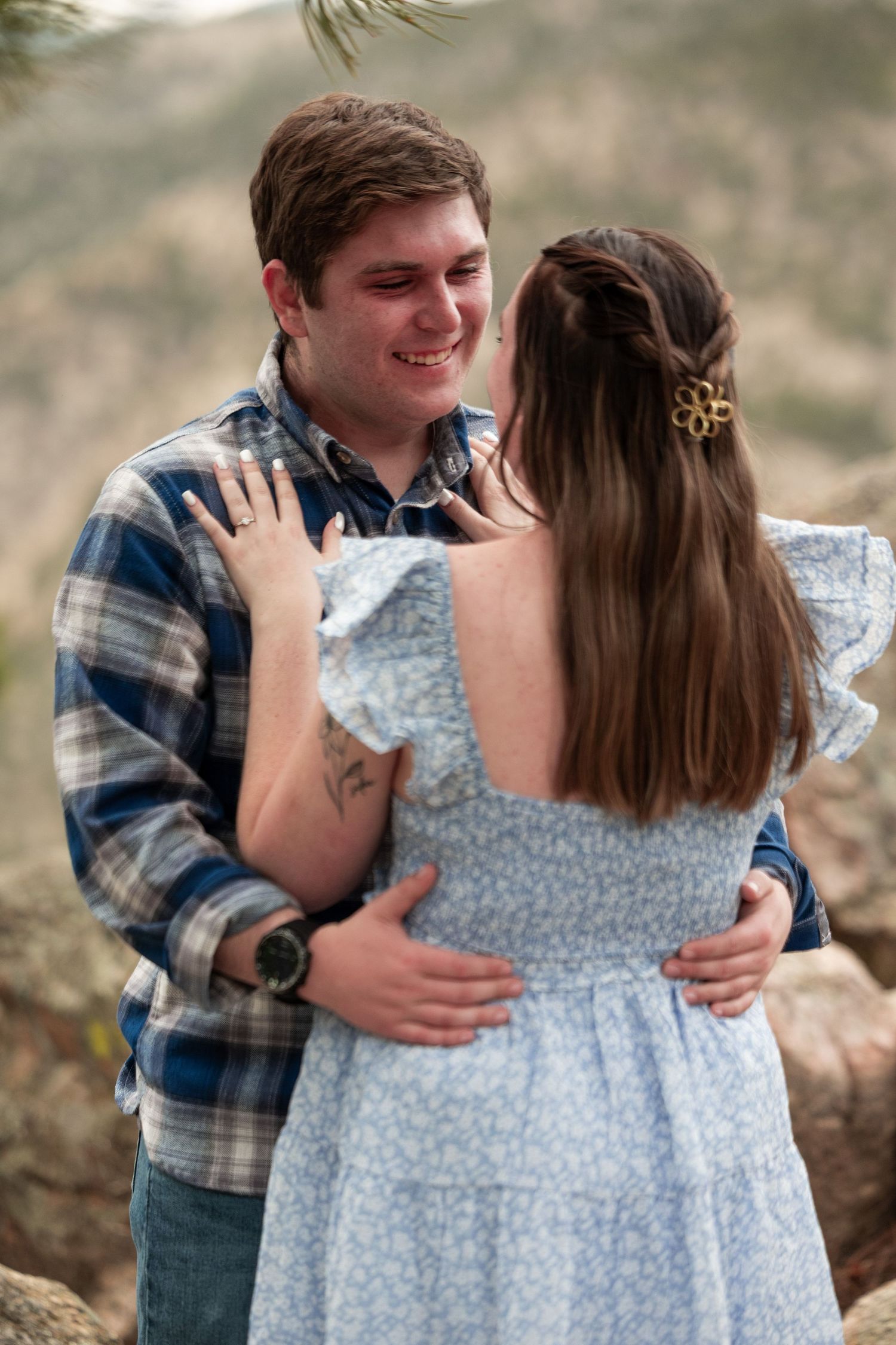 Couple sharing tender embrace outdoors wearing blue plaid and floral dress.