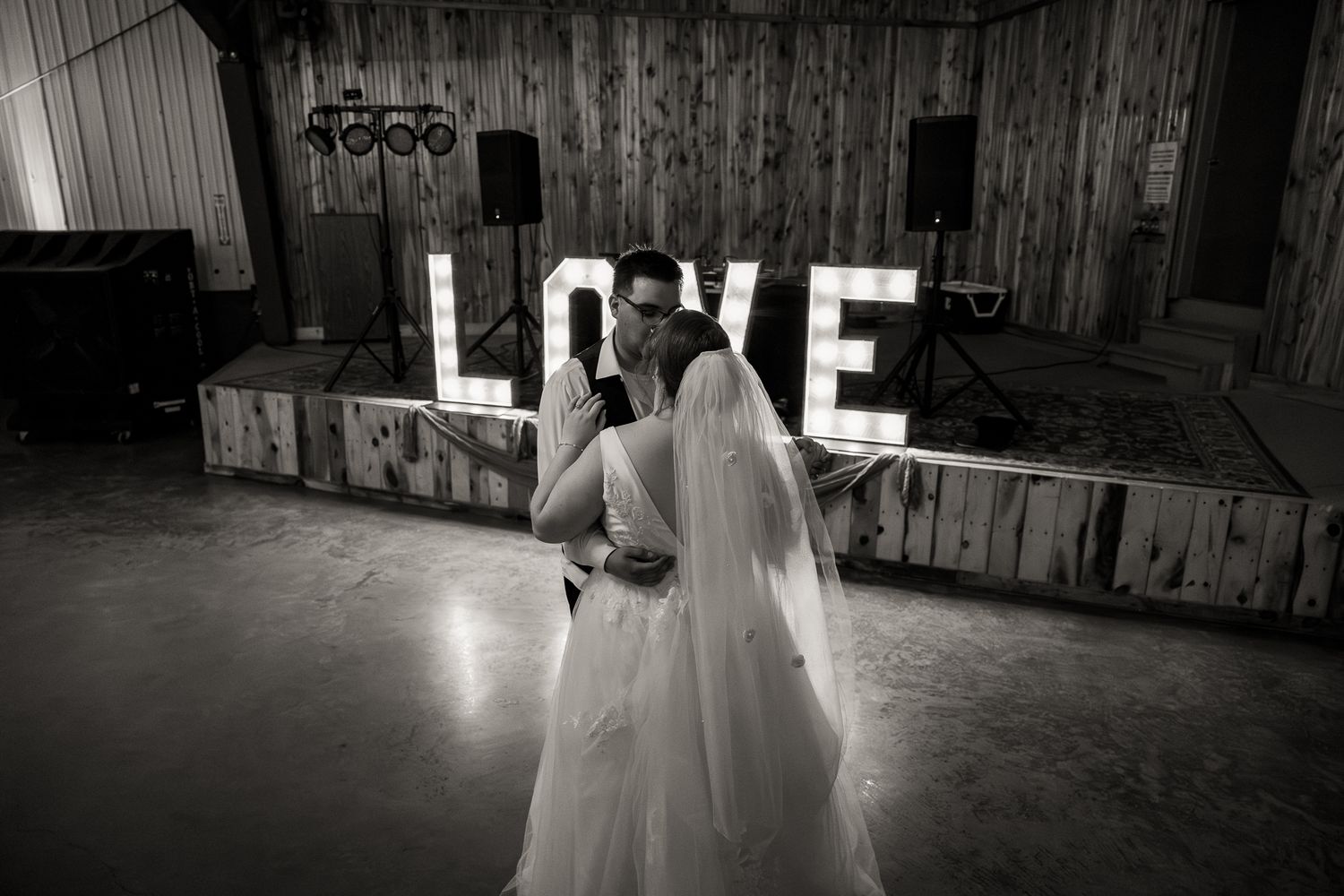 Bride and groom share first dance in front of illuminated LOVE sign at wedding reception.