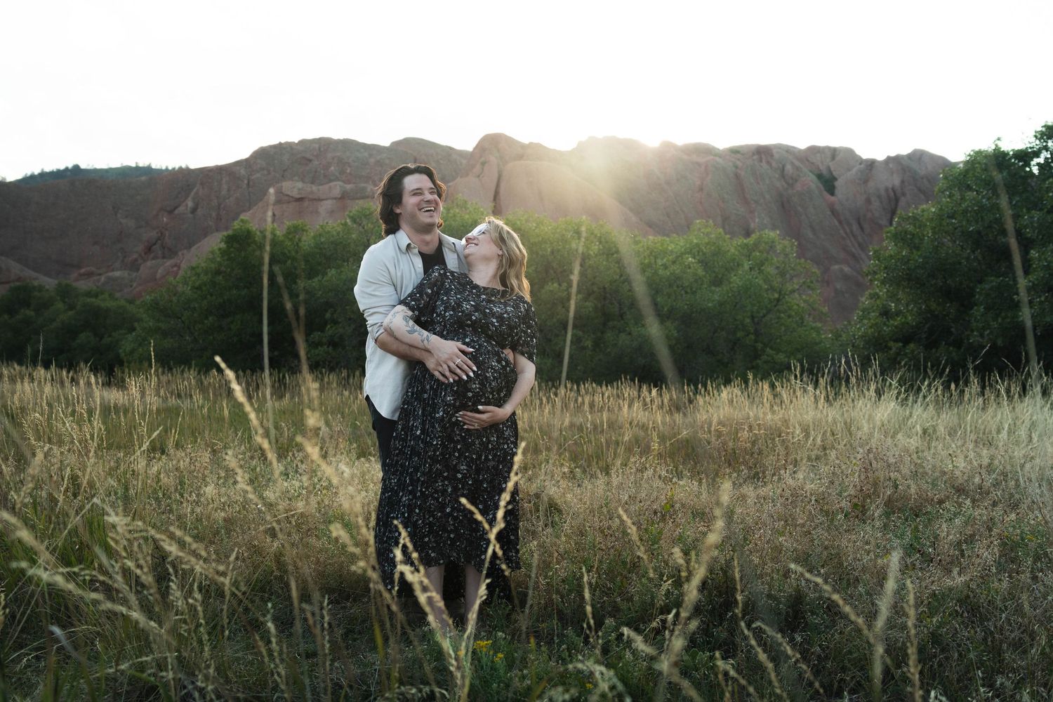 Scenic view of people walking through meadow with mountains and sunset in background.