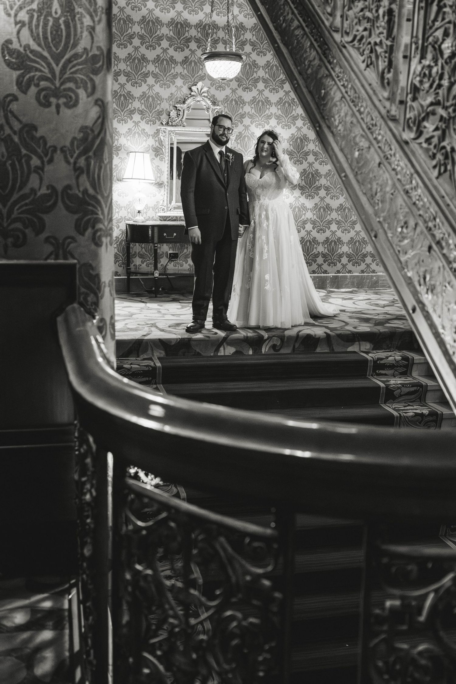 A black and white photo of newlyweds on an ornate vintage staircase.