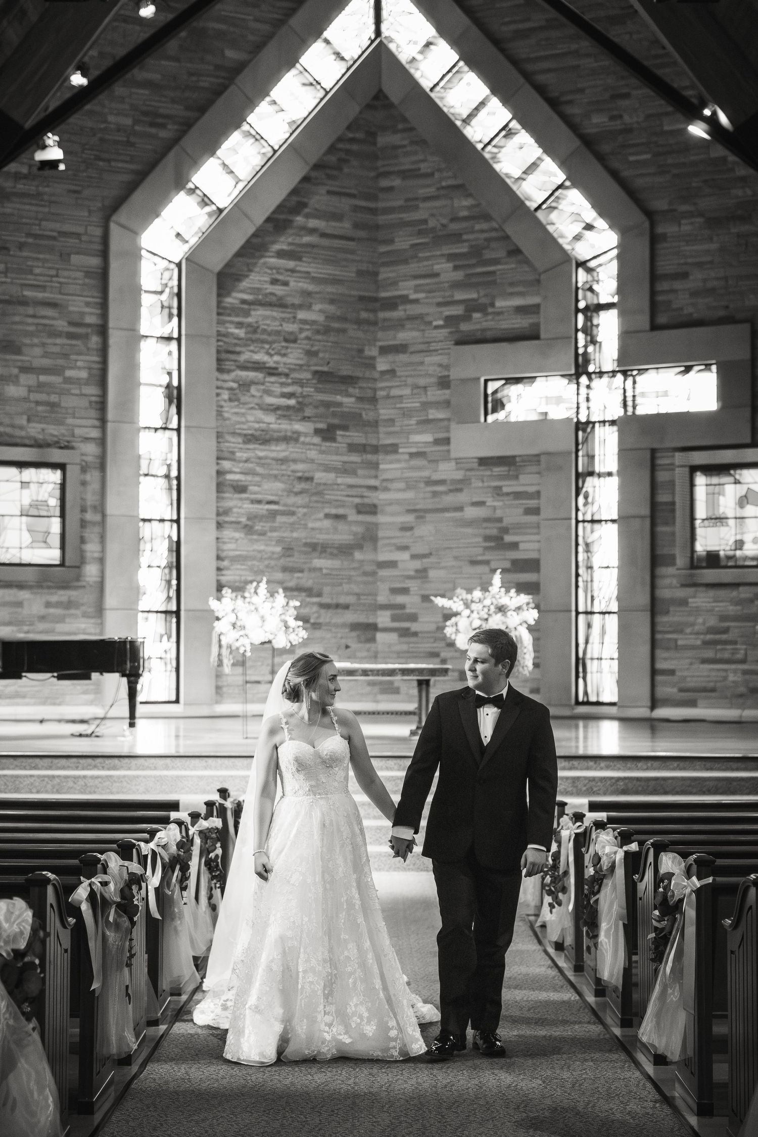 Black and white photo of bride and groom holding hands walking down church aisle after wedding ceremony.