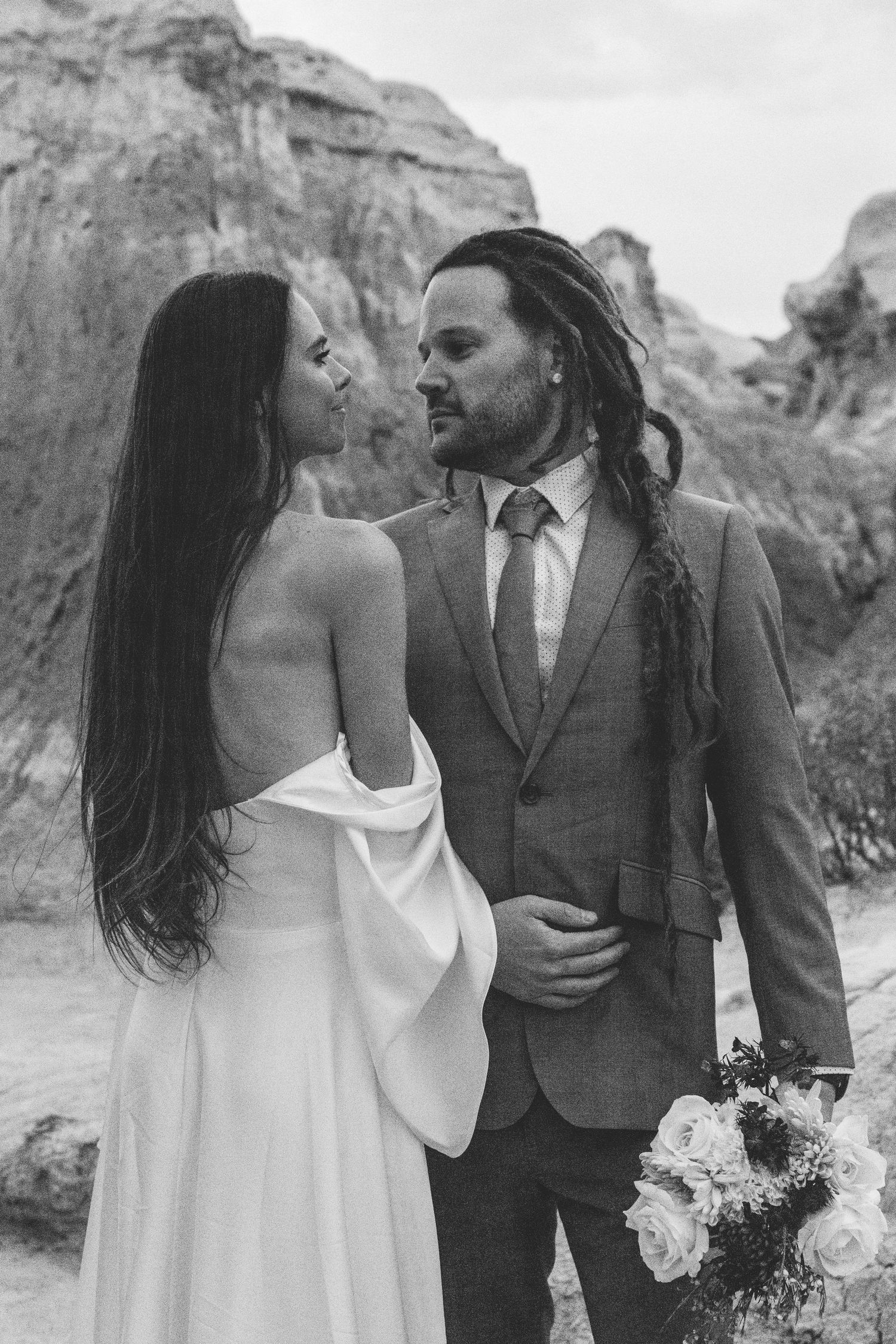 Romantic wedding portraits in black and white showing intimate moments against desert cliffs.