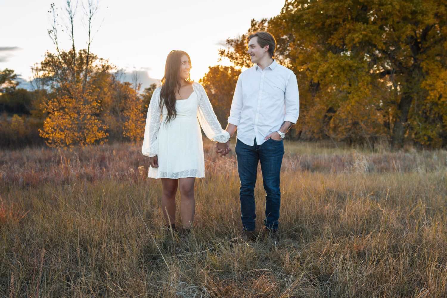 Young couple holding hands while walking through autumn field at sunset.