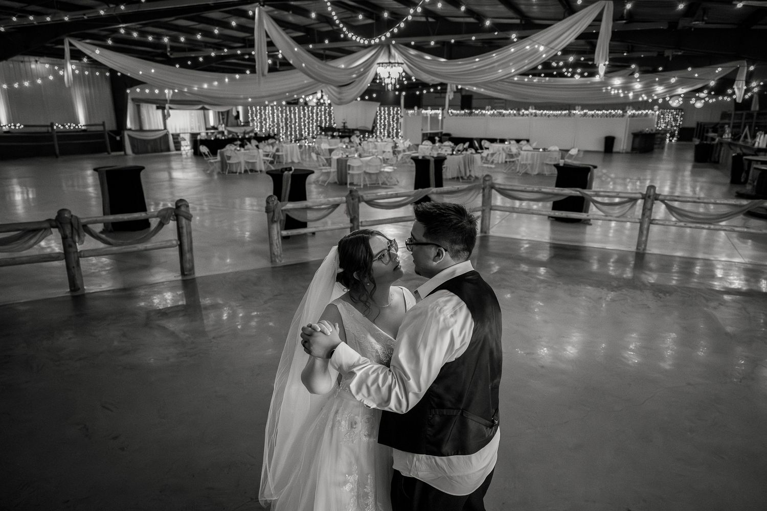 Black and white photo of bride and groom sharing first dance in elegant decorated wedding reception venue.