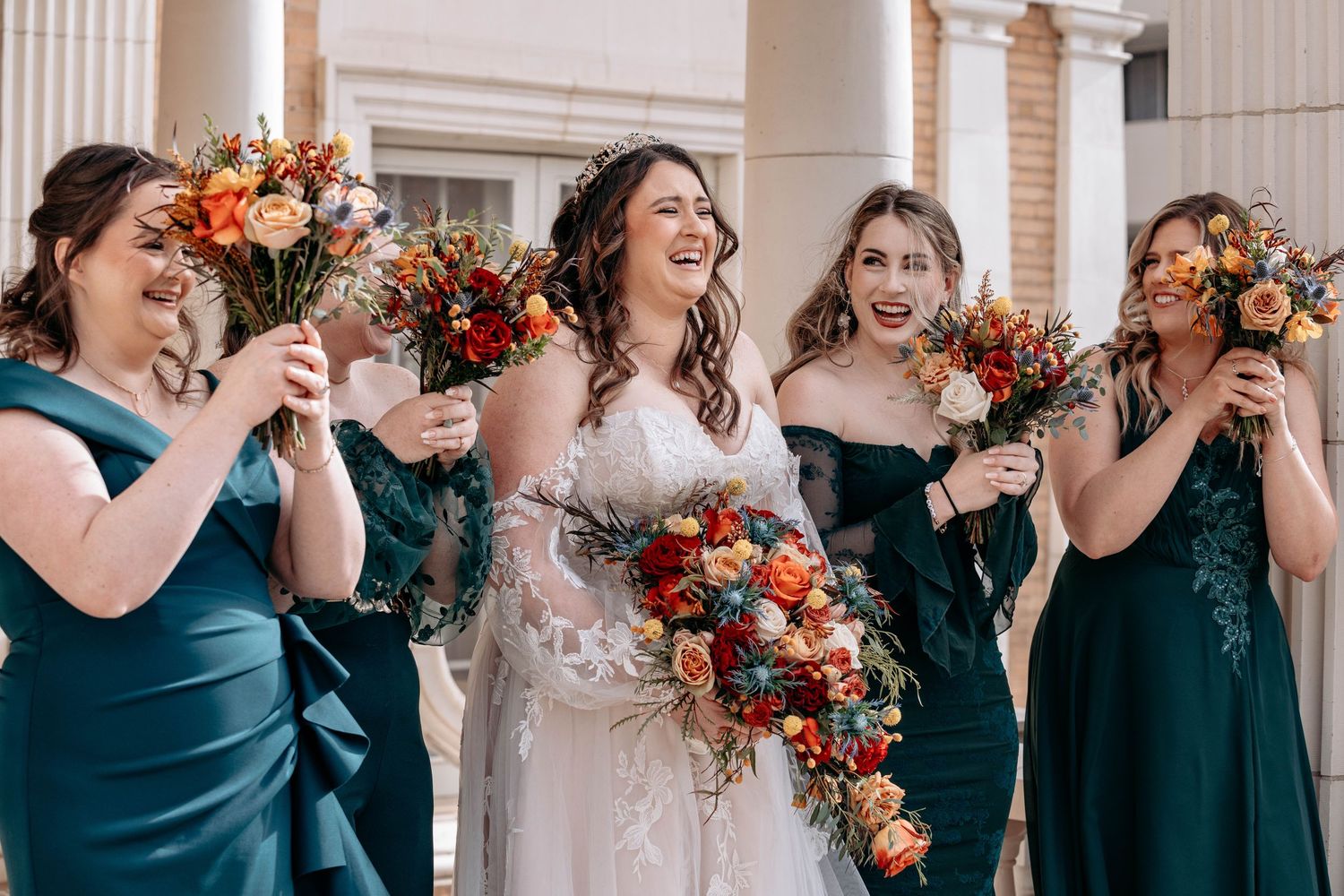 Wedding party in navy dresses and autumn florals laughing together.