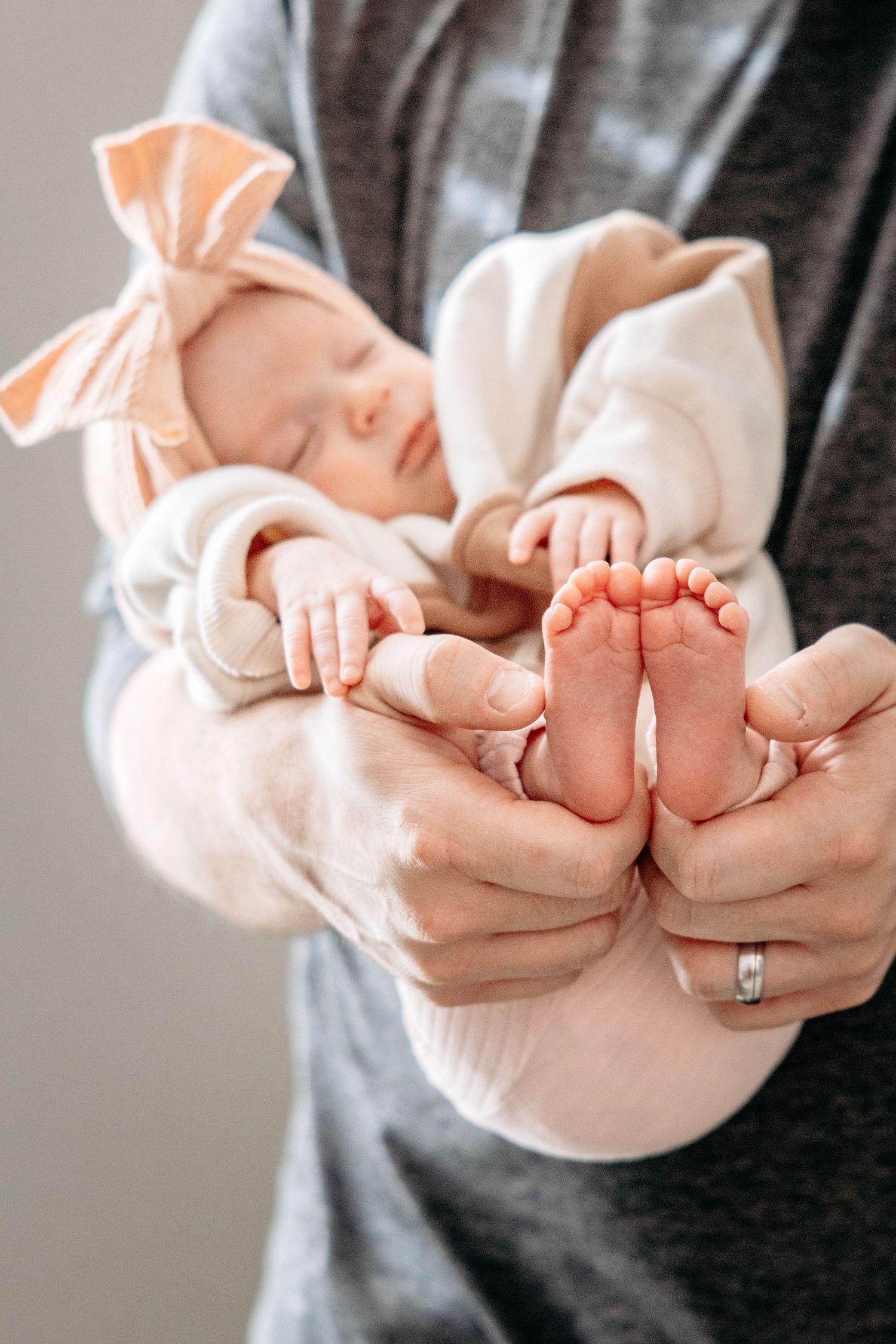 Close-up of tiny baby feet being held by adult hands, with a pink bow visible.