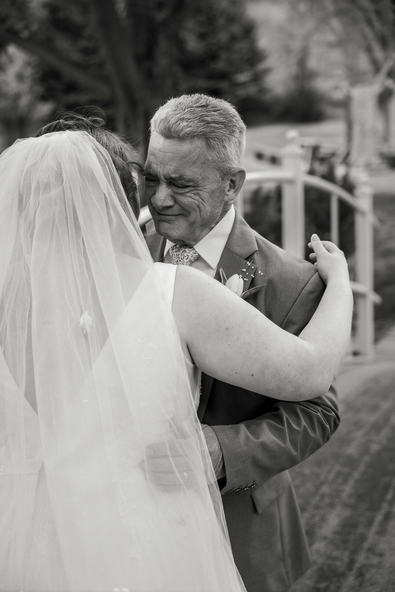 Emotional black and white photo of a bride hugging an older man in a suit, likely her father, at a wedding.