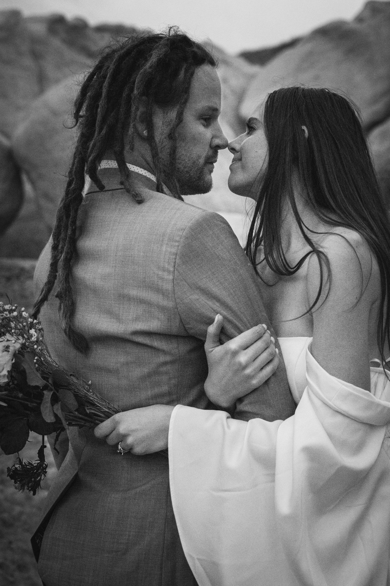 An intimate black and white portrait of newlyweds sharing a close moment among desert rocks.
