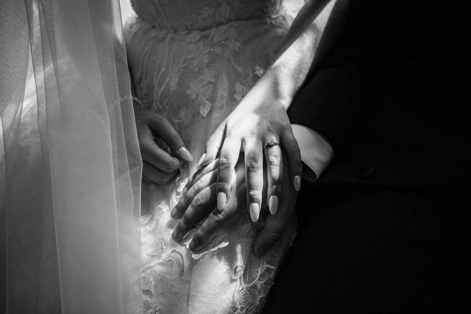 Black and white close-up of newlyweds hands with wedding rings, bride in lace dress.