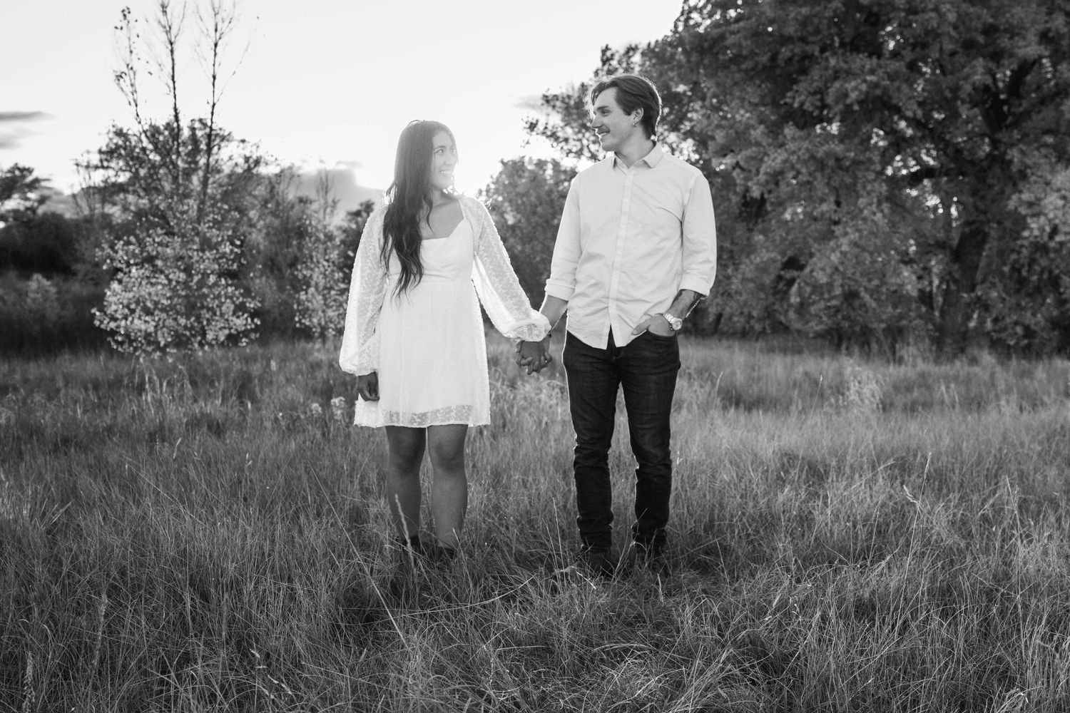 A couple holding hands while walking through a meadow in black and white photography.