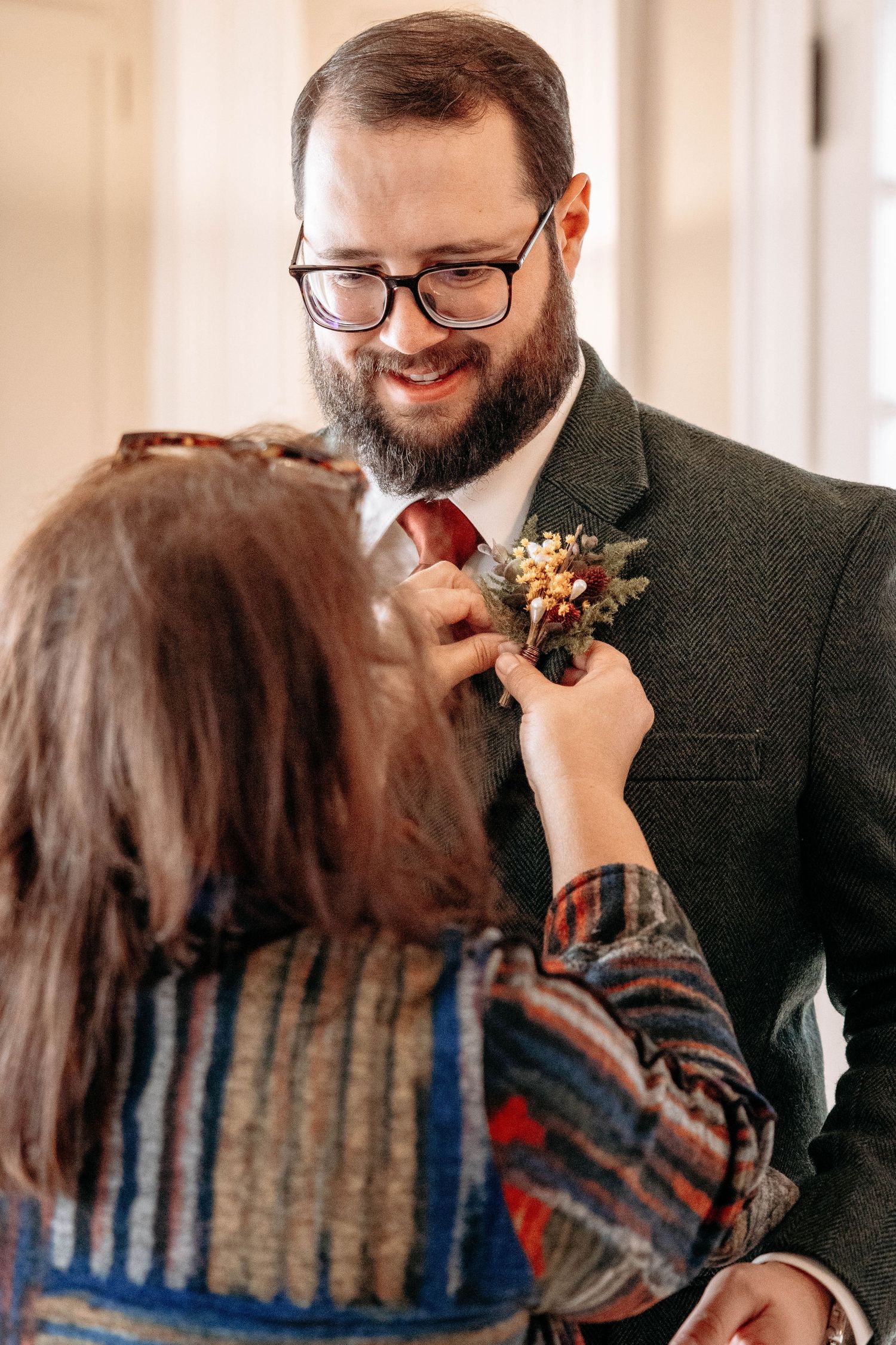 A boutonniere is pinned onto a green suit jacket during wedding preparations.