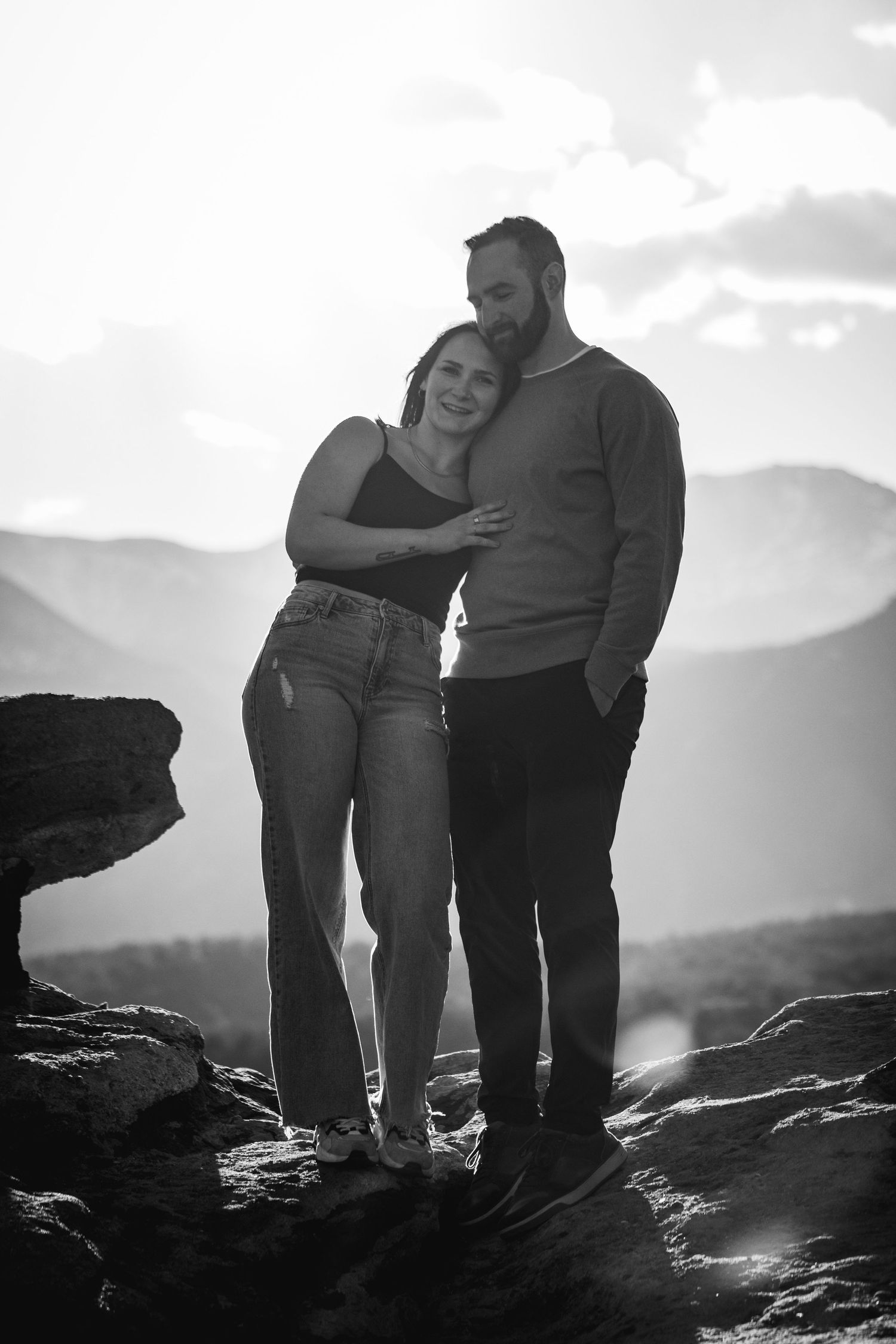 Black and white silhouettes of couple embracing on rocky mountain overlook.