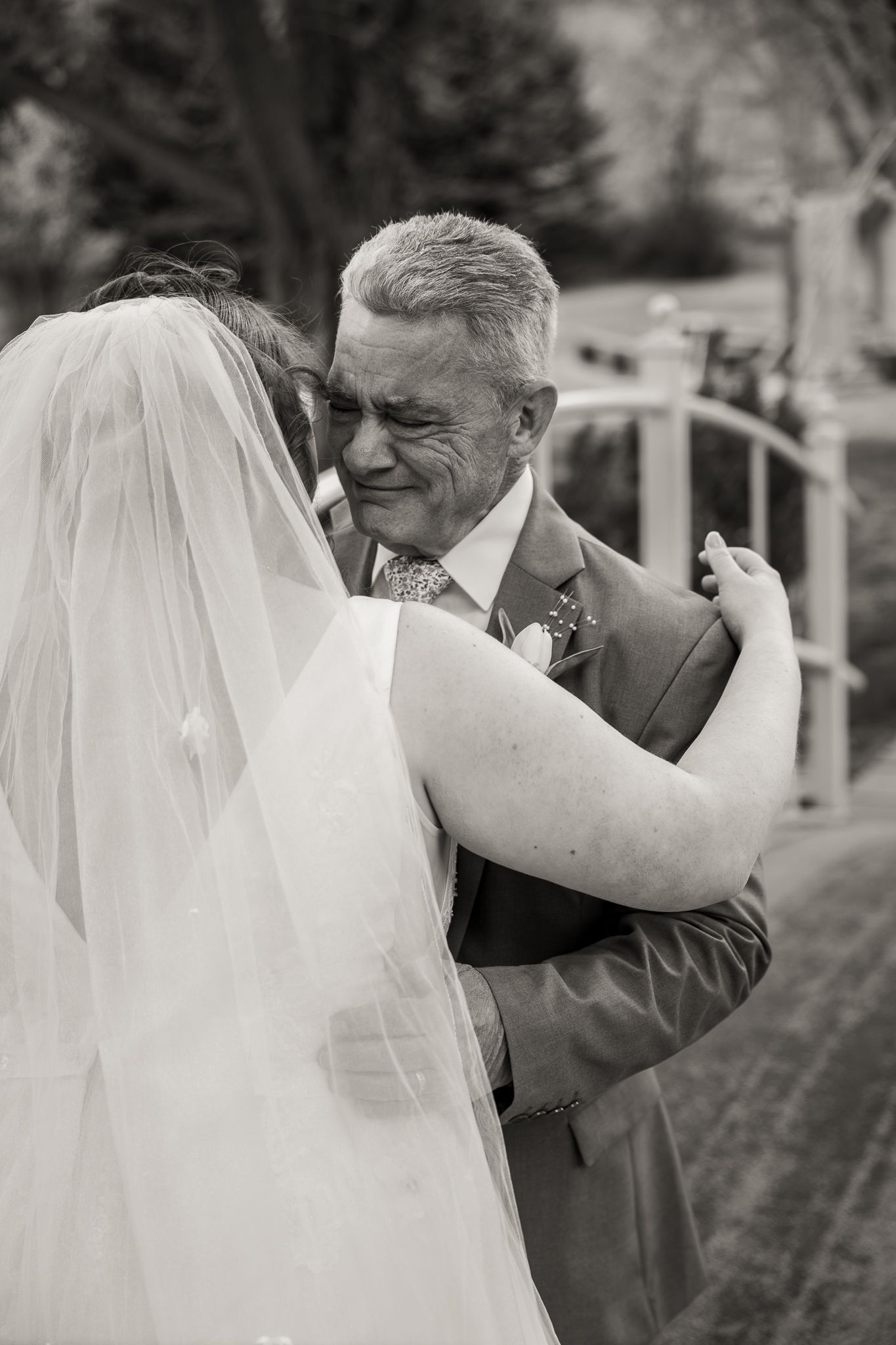 Black and white photo of emotional father hugging bride in wedding veil, sharing tender moment outdoors.