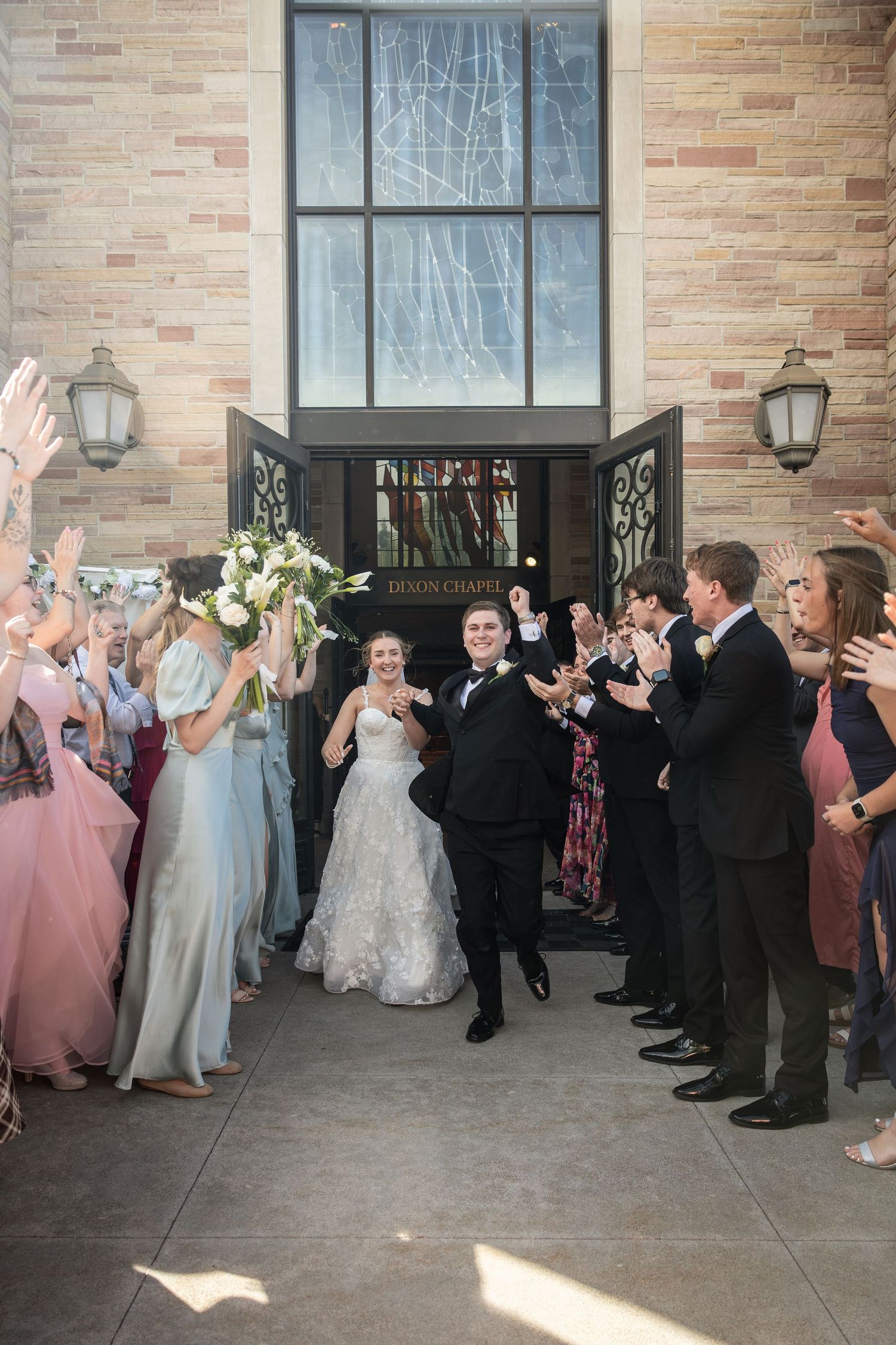 Bride and groom exit Lemon Chapel wedding ceremony through cheering guests in formal attire on sunny day.