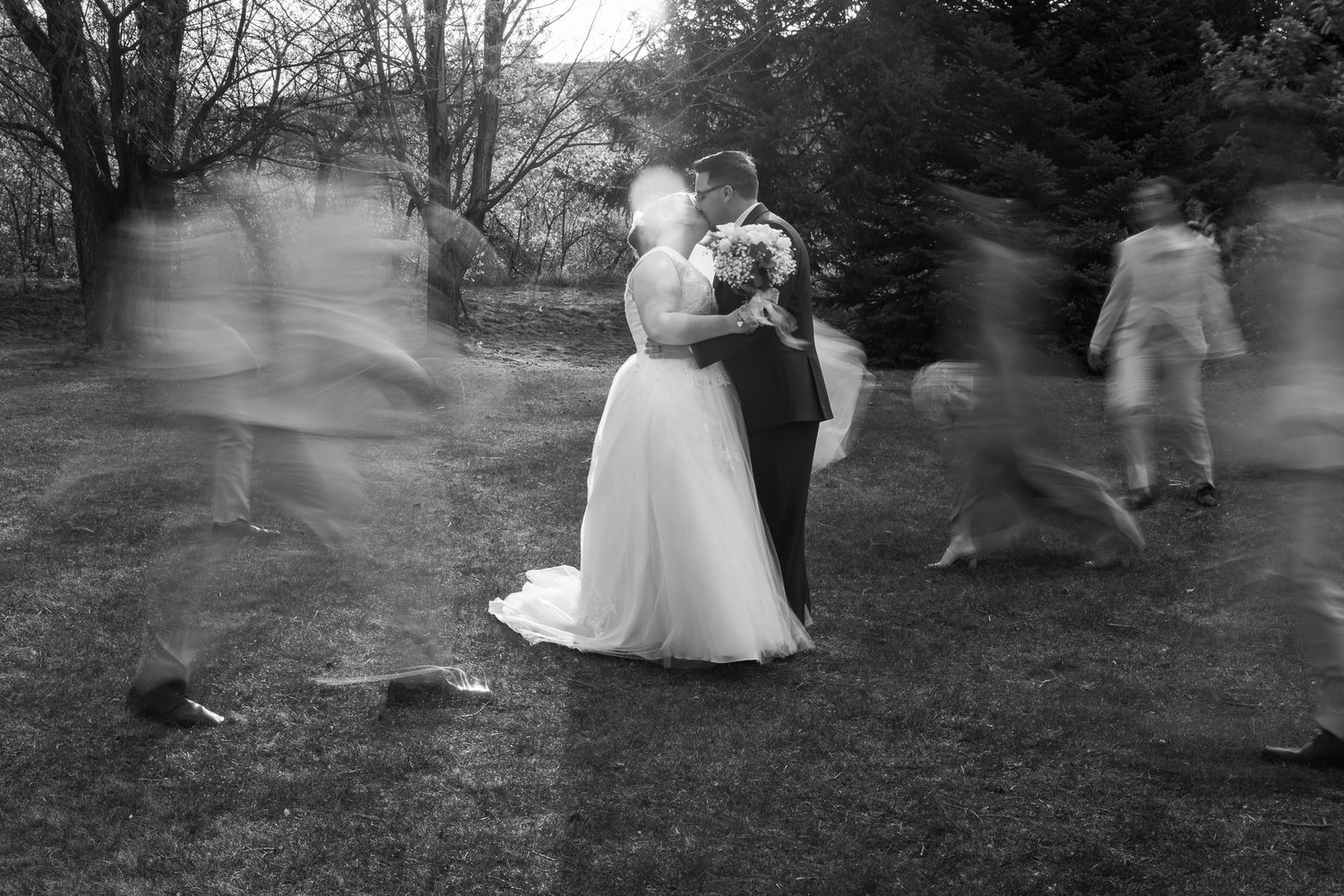 Black and white photo of bride and groom embracing while wedding guests move around them in a blur.