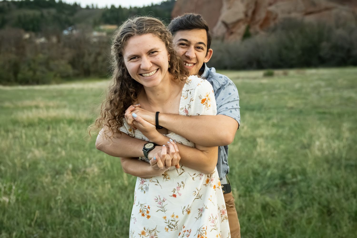 Happy couple embracing in a green meadow with red rock formations in the background during golden hour.