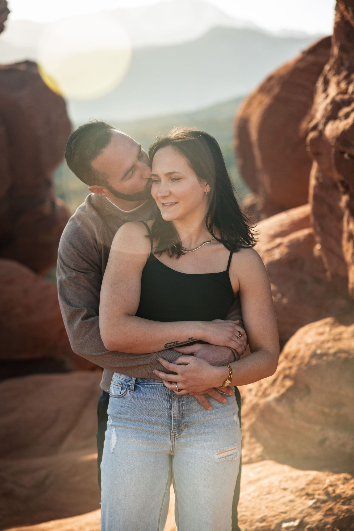 Romantic couple embracing against red rock formations at sunset.