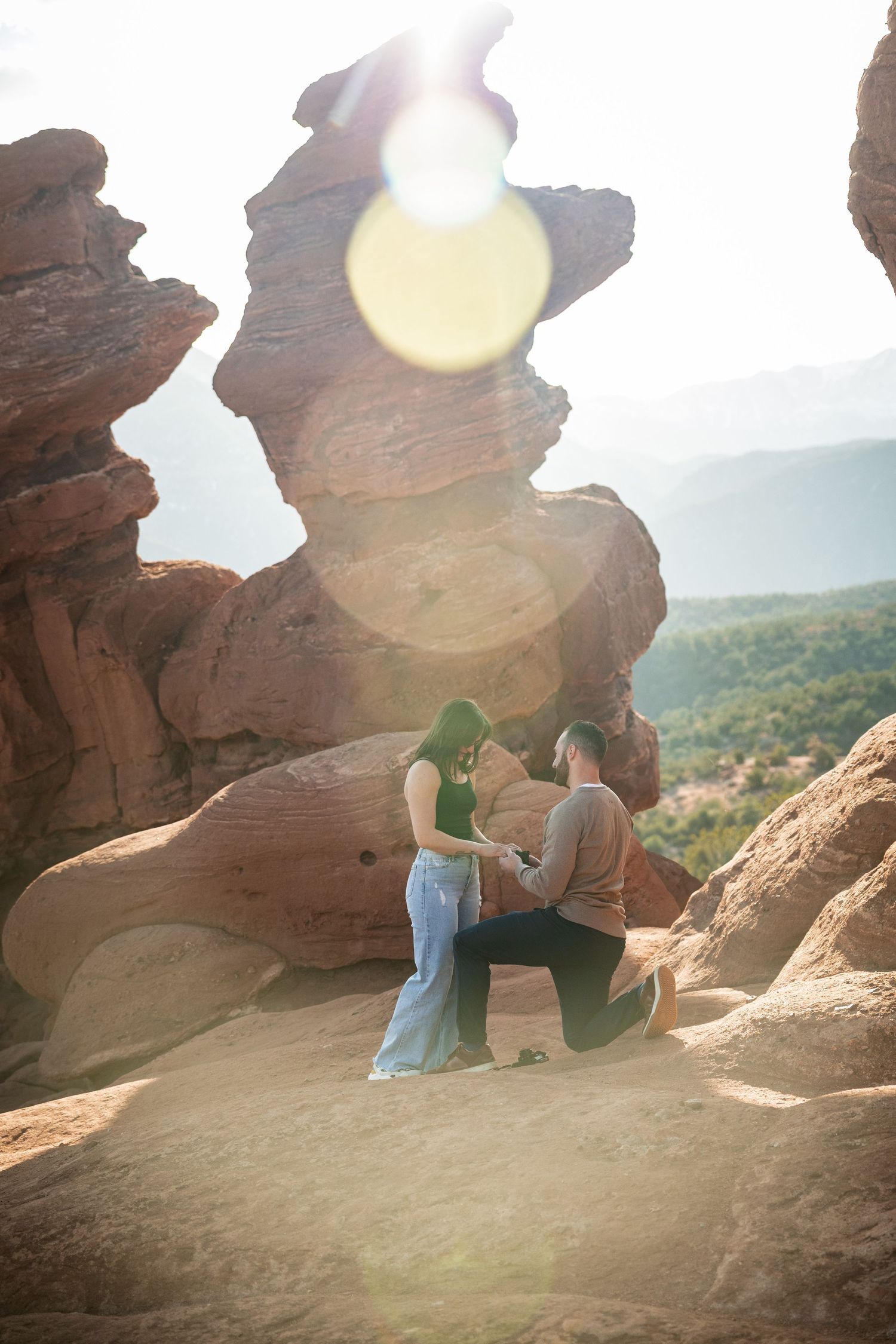 Sun-lit engagement photos taken at red rock formations with scenic valley views.