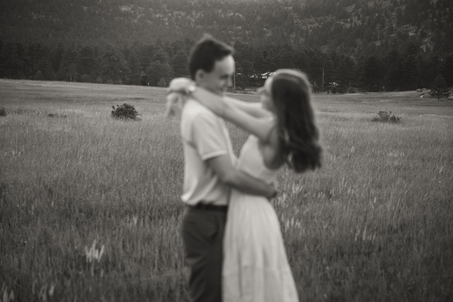 Black and white photo of a couple dancing romantically in a lush green meadow field.