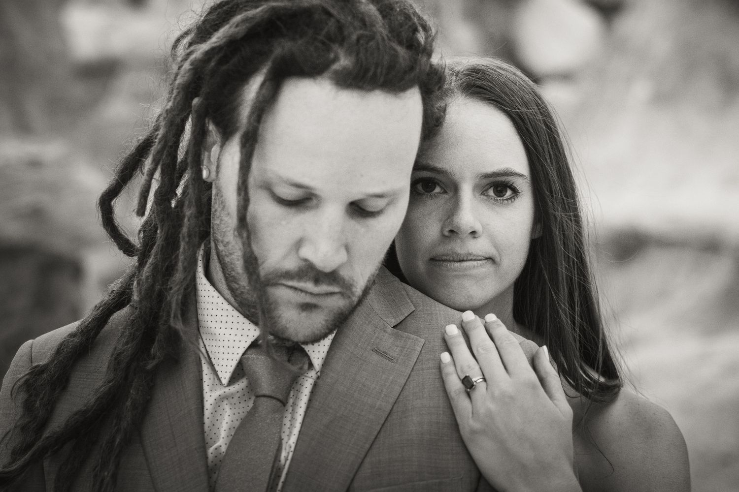 Black and white portrait of a couple, man with dreadlocks in suit, woman showing engagement ring, romantic photo.