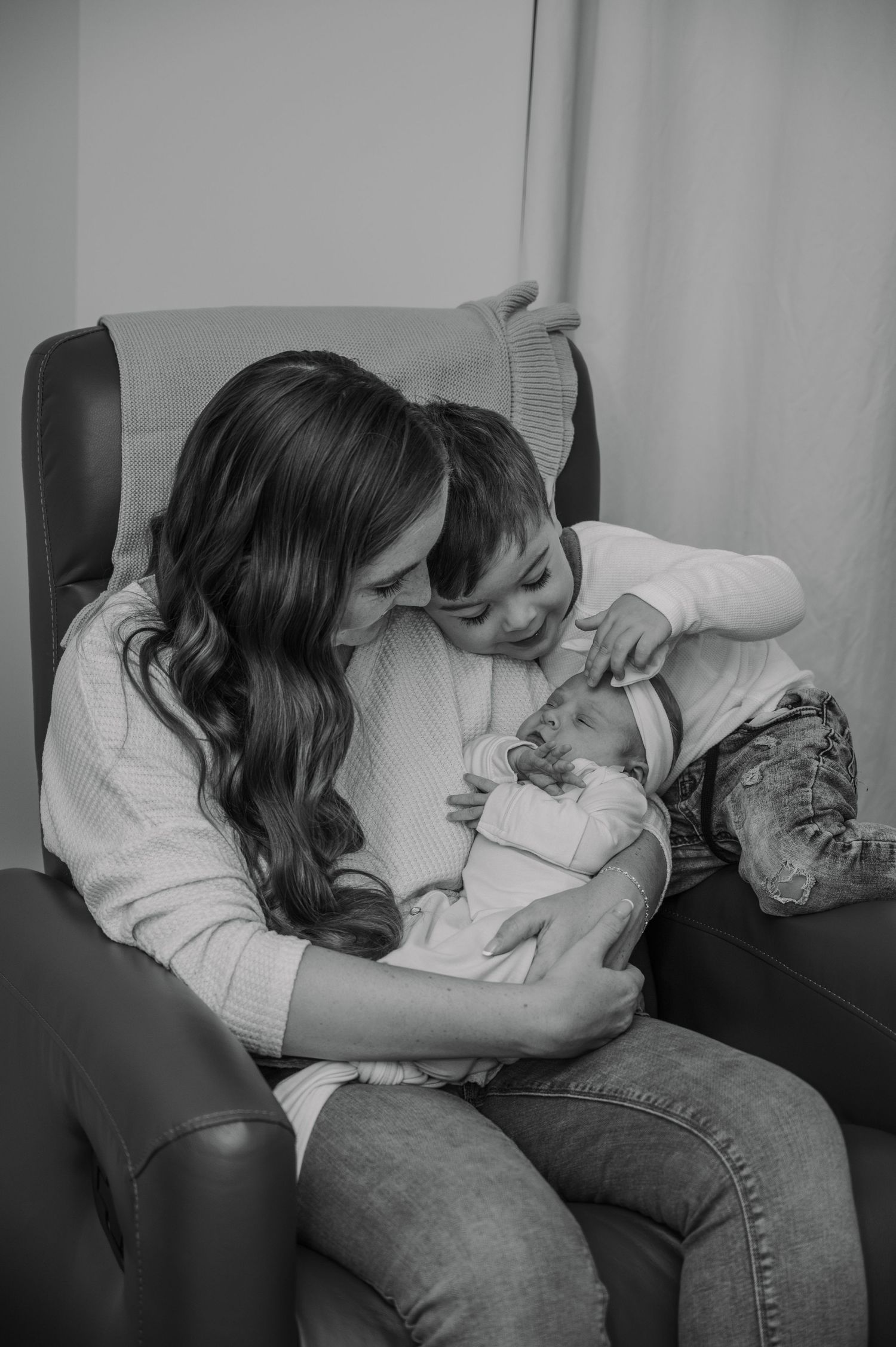 A series of black and white photos showing a mom with her oldest child and newborn cuddling on a rocking chair.