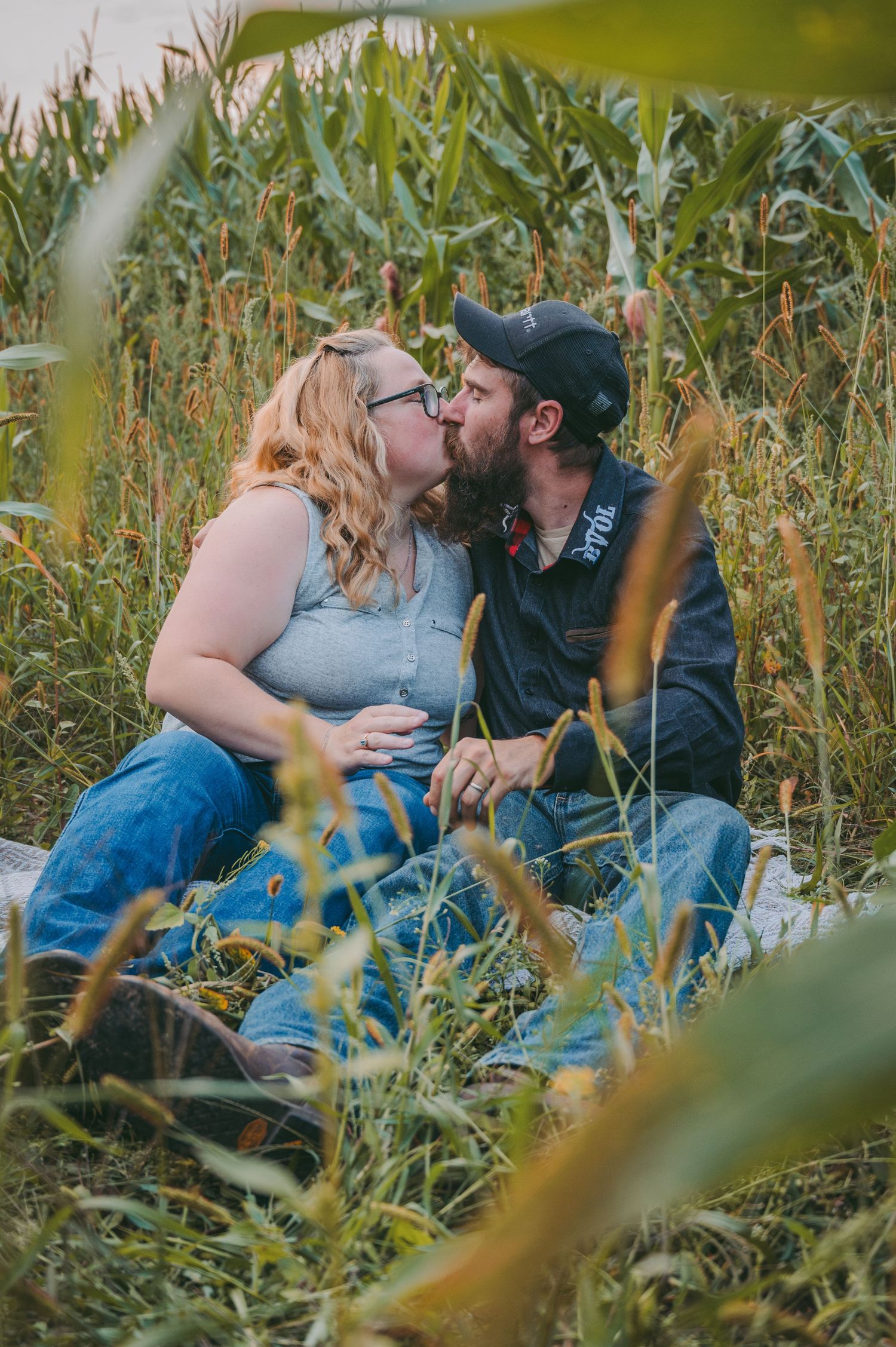 An intimate moment shared between a couple sitting in a cornfield during golden hour.