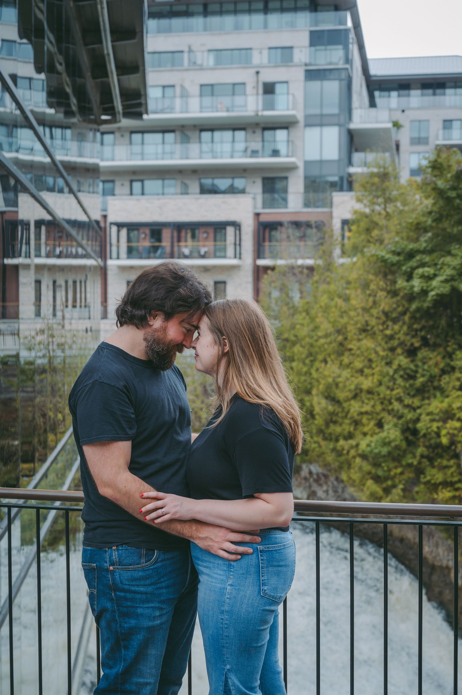 A romantic couple embraces on an urban balcony with modern apartment buildings in the background.