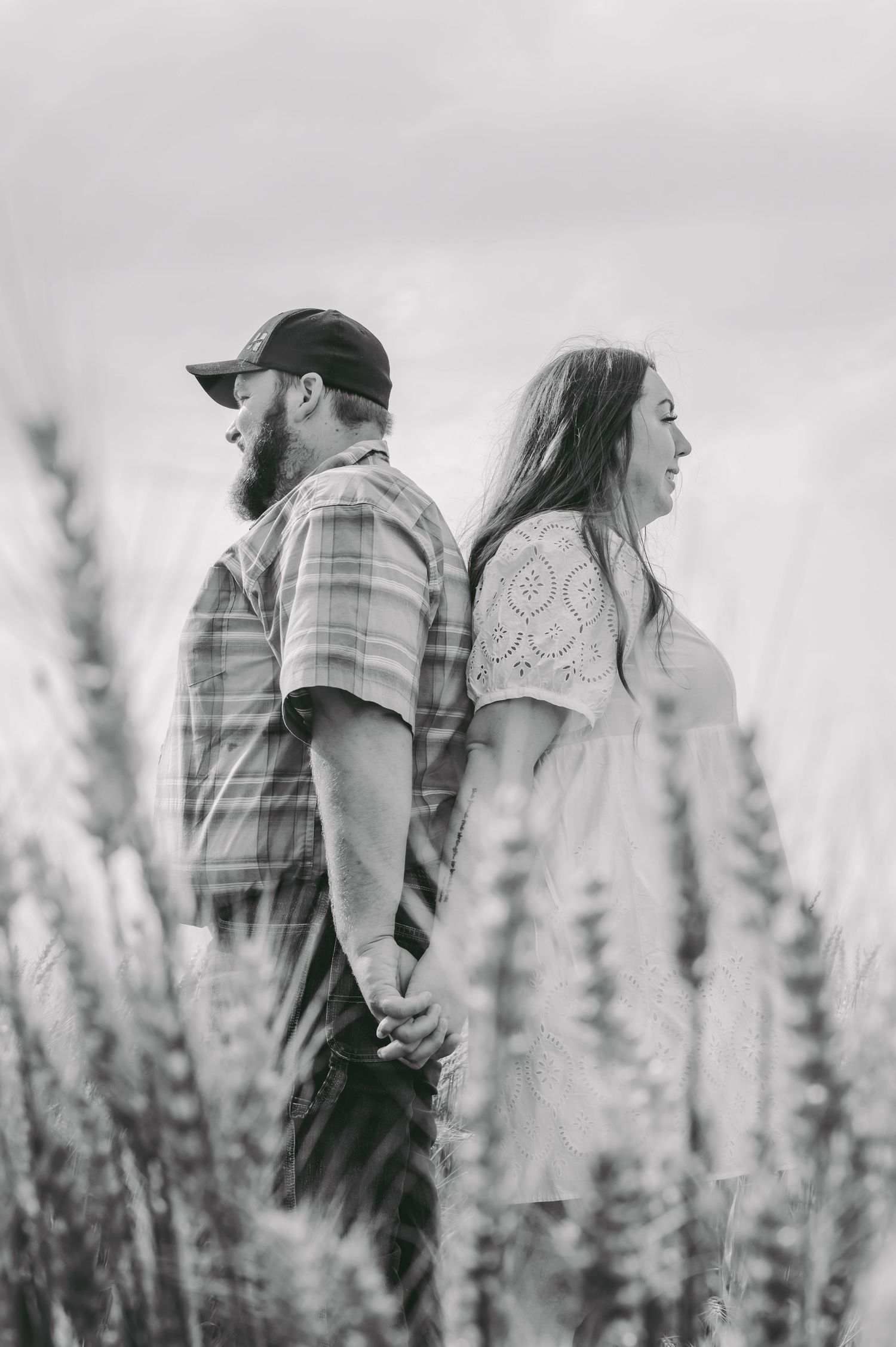 A black and white portrait of a couple standing back-to-back in a wheat field.