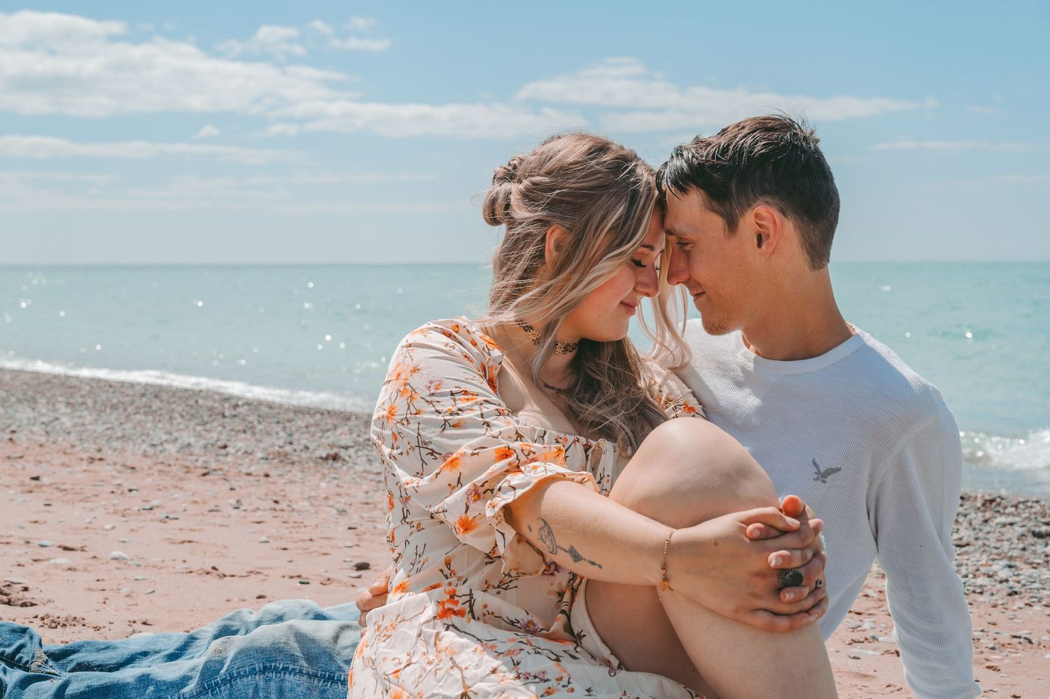 A tender beach moment between a couple sitting on a blanket by the ocean.