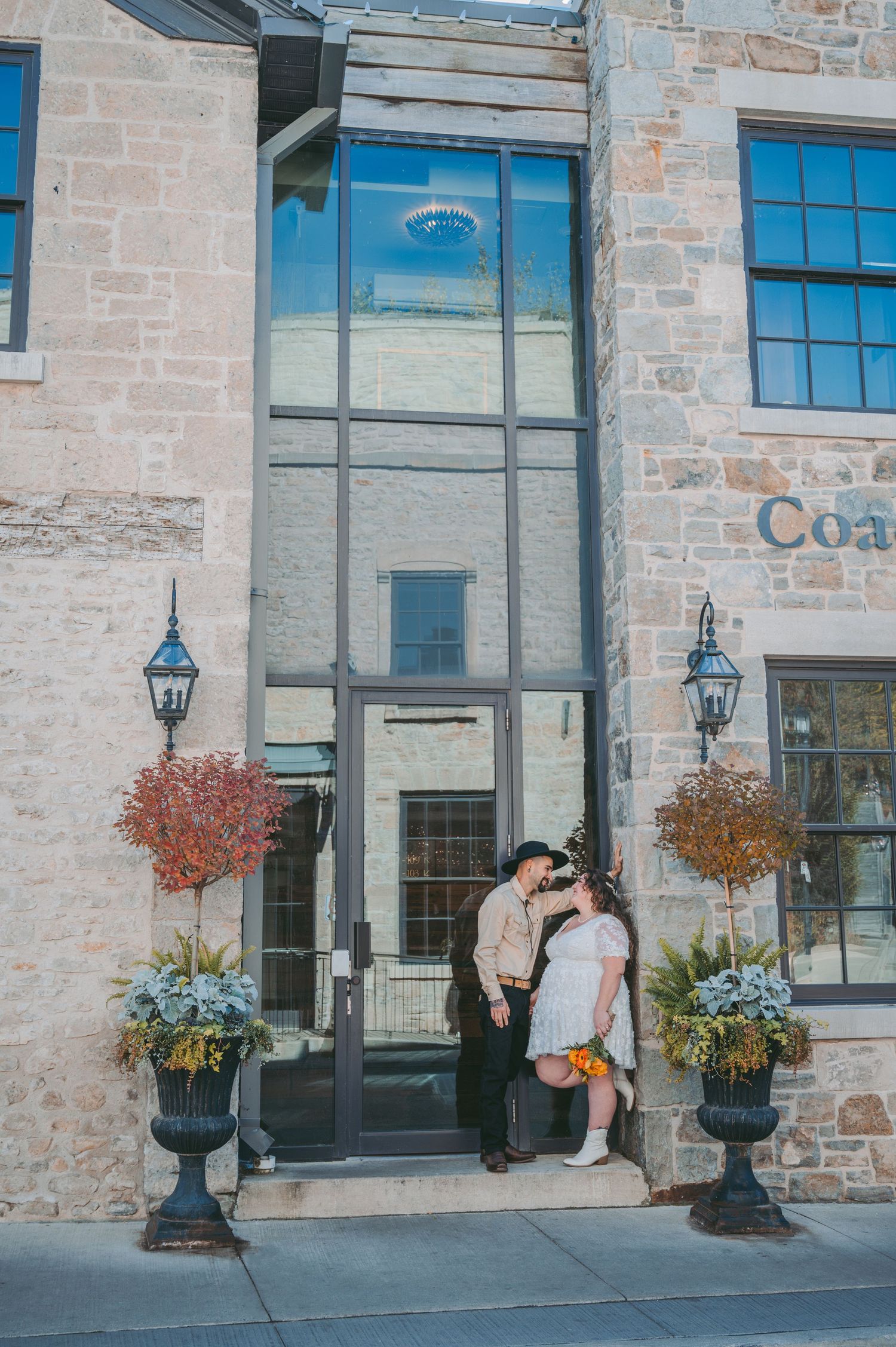Couple poses romantically on stone steps of historic building with decorative planters.