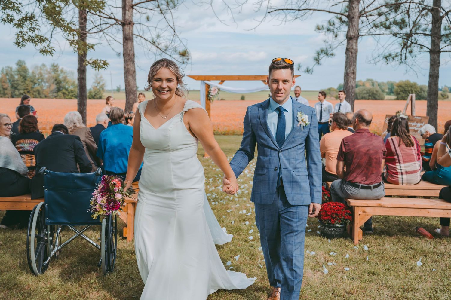 A couple walks joyfully down the aisle at an outdoor wedding ceremony with guests seated on wooden benches.