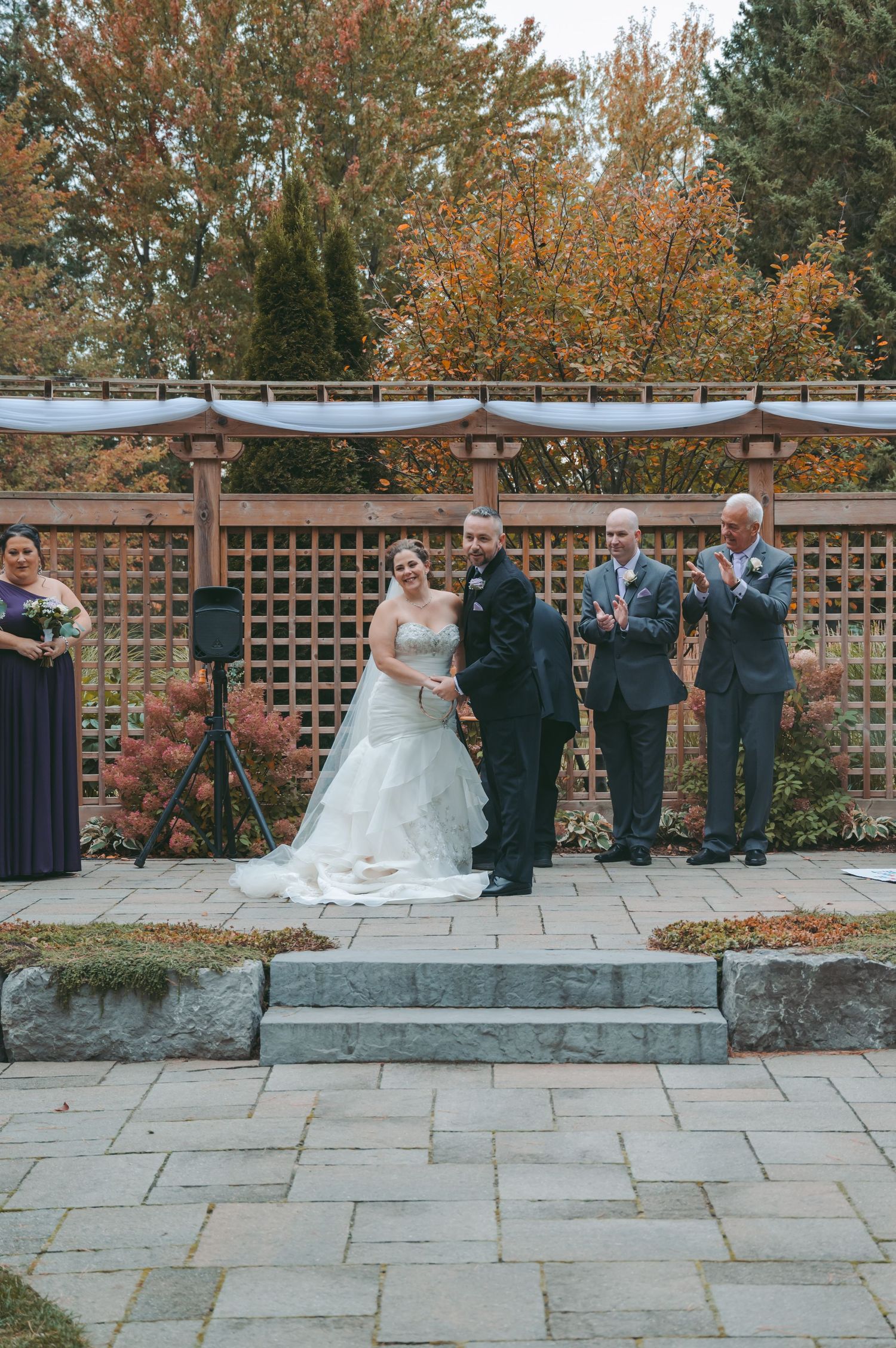 A wedding ceremony under a pergola with autumn colors in the background.