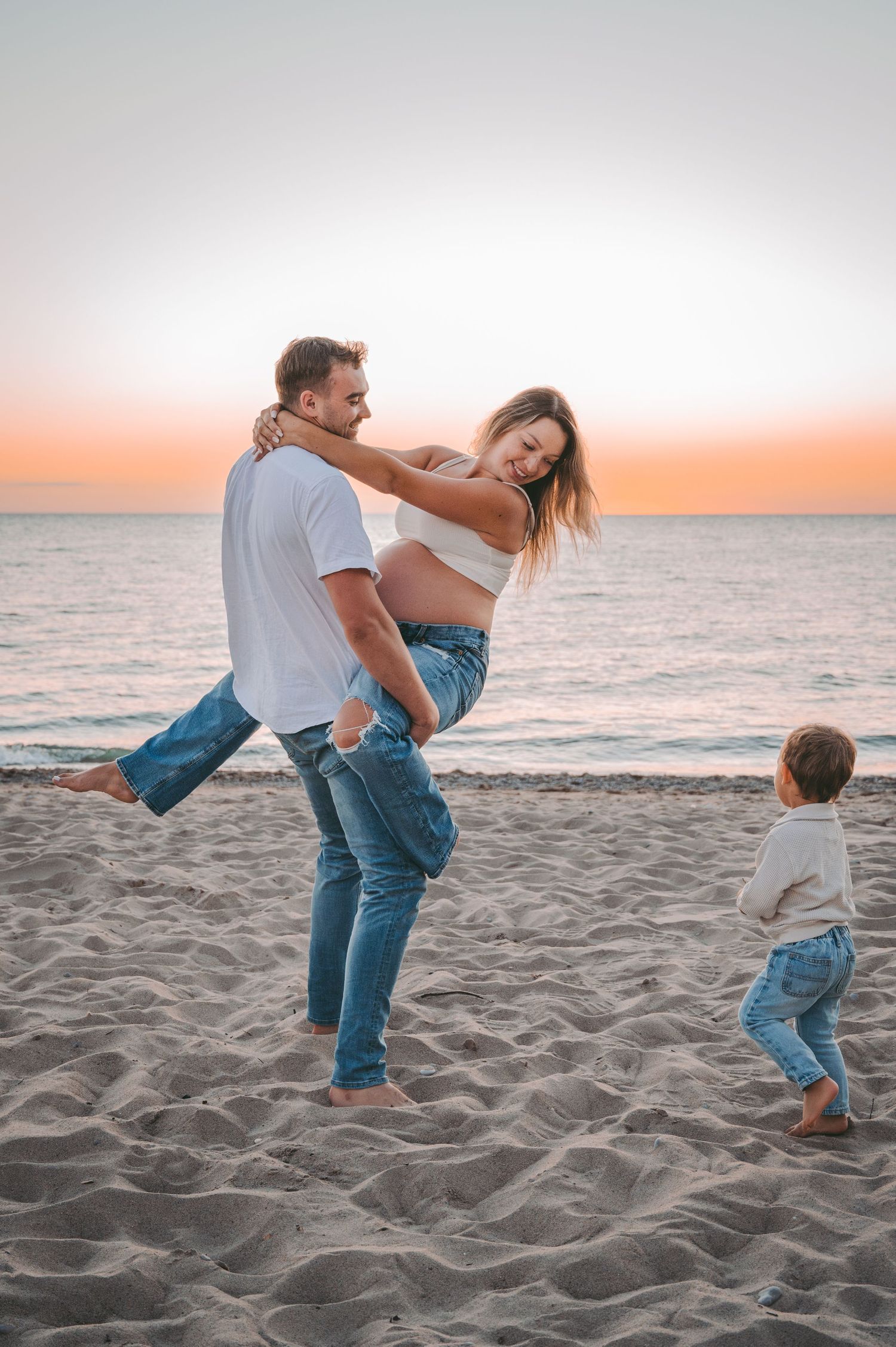 A family plays together on a sandy beach at sunset, with waves and orange sky in the background.
