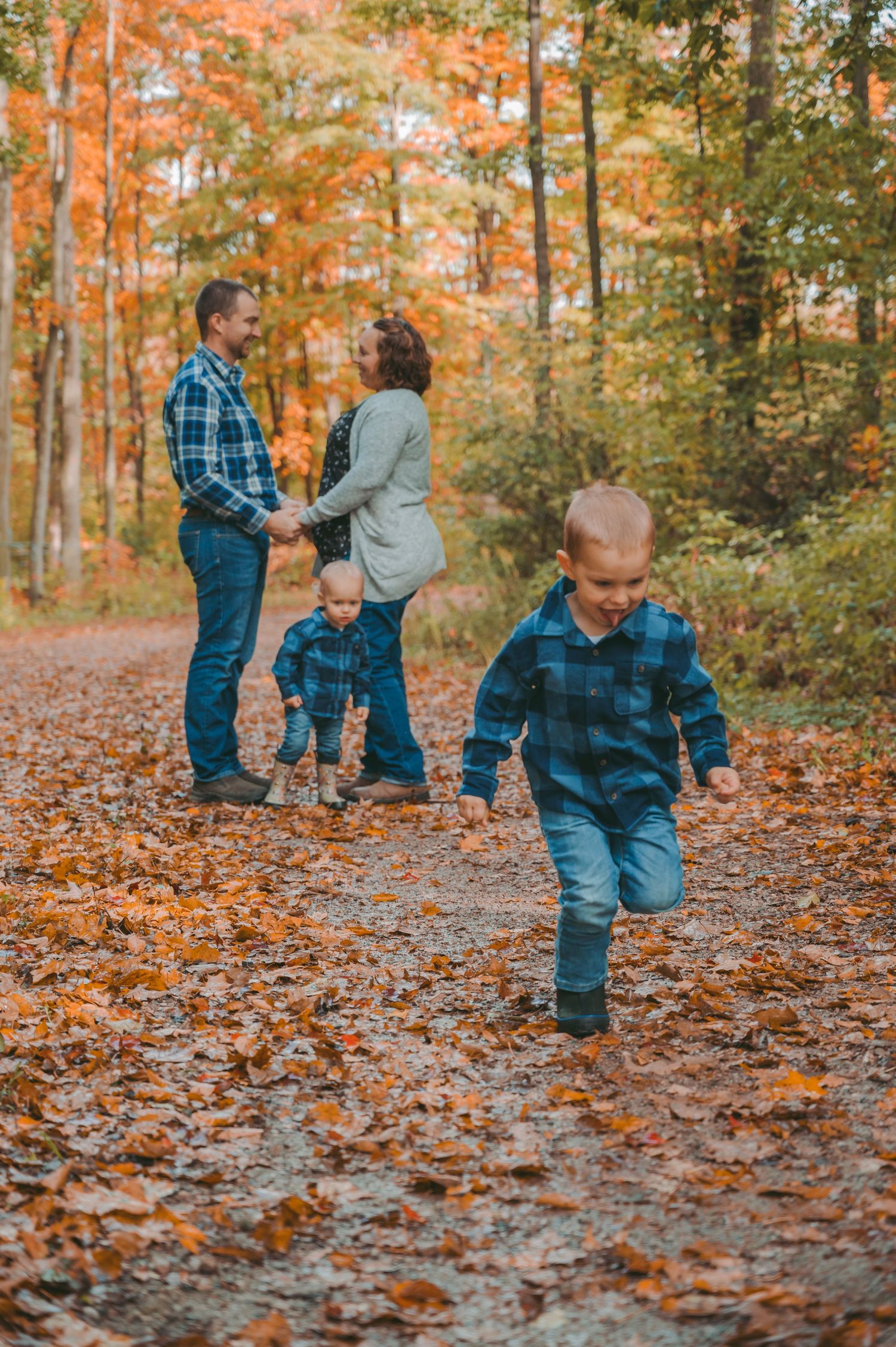 Family enjoying an autumn walk on a leaf-covered trail in the woods with vibrant fall foliage.