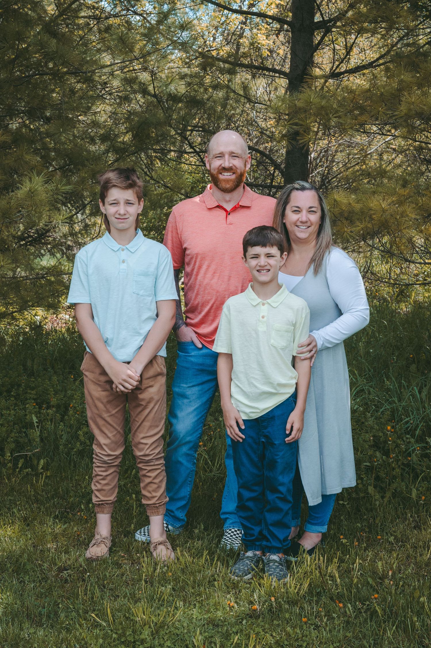 Family of four poses outdoors against pine trees in coordinated outfits.