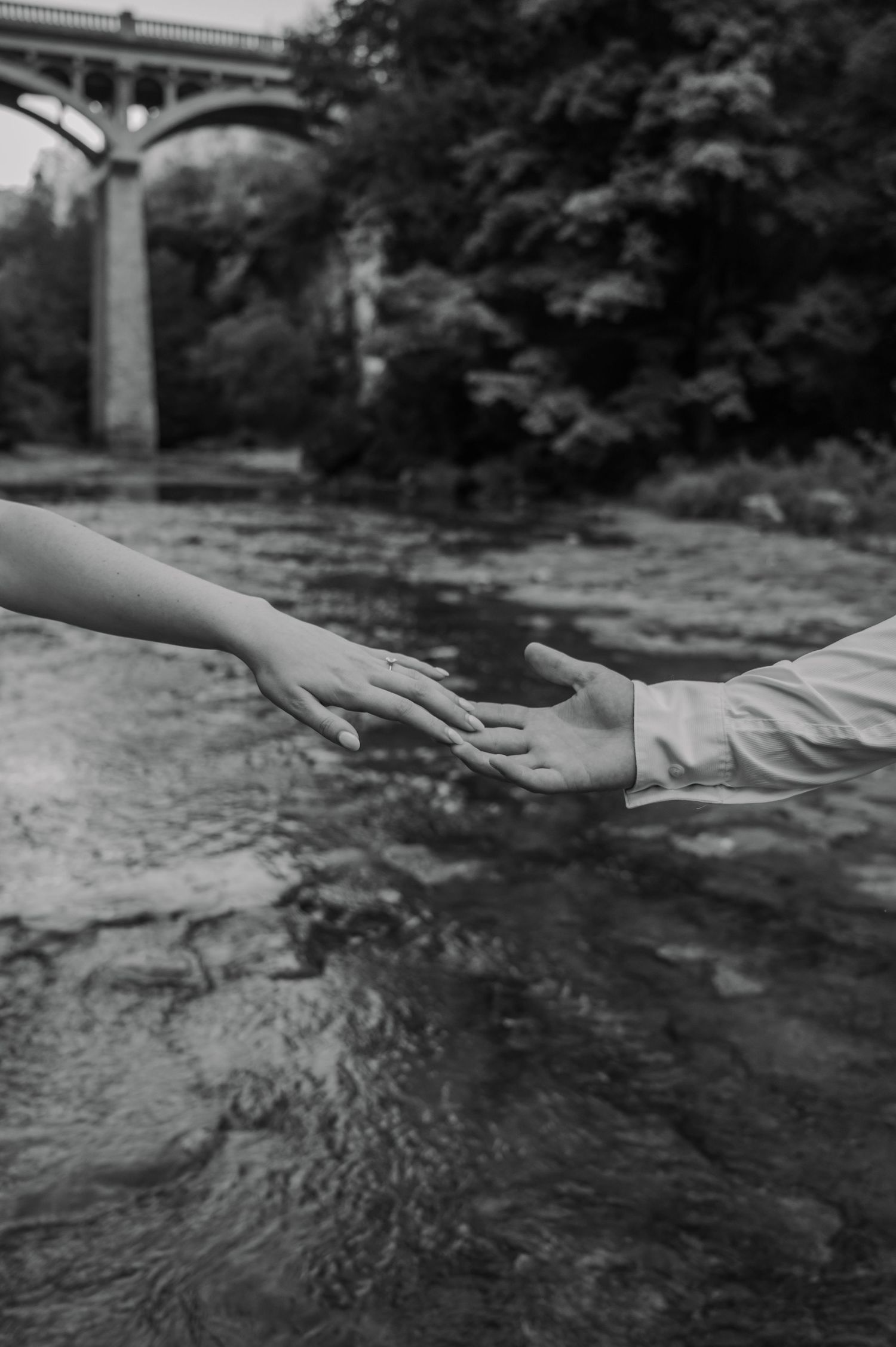 A sequence of black and white photographs showing hands gently touching and interacting with flowing water in a stream.