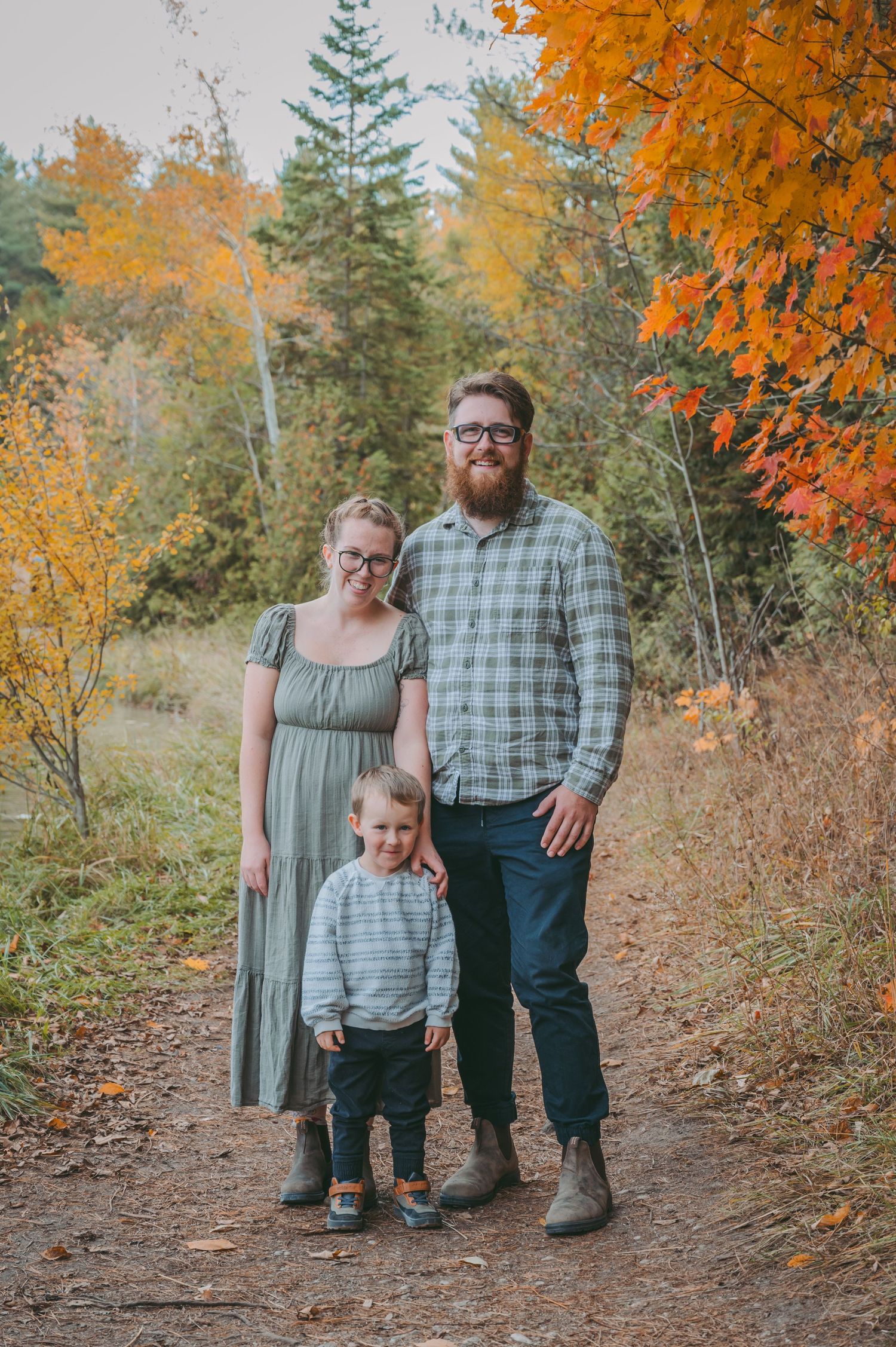 Family poses for portrait on forest trail surrounded by vibrant fall foliage.