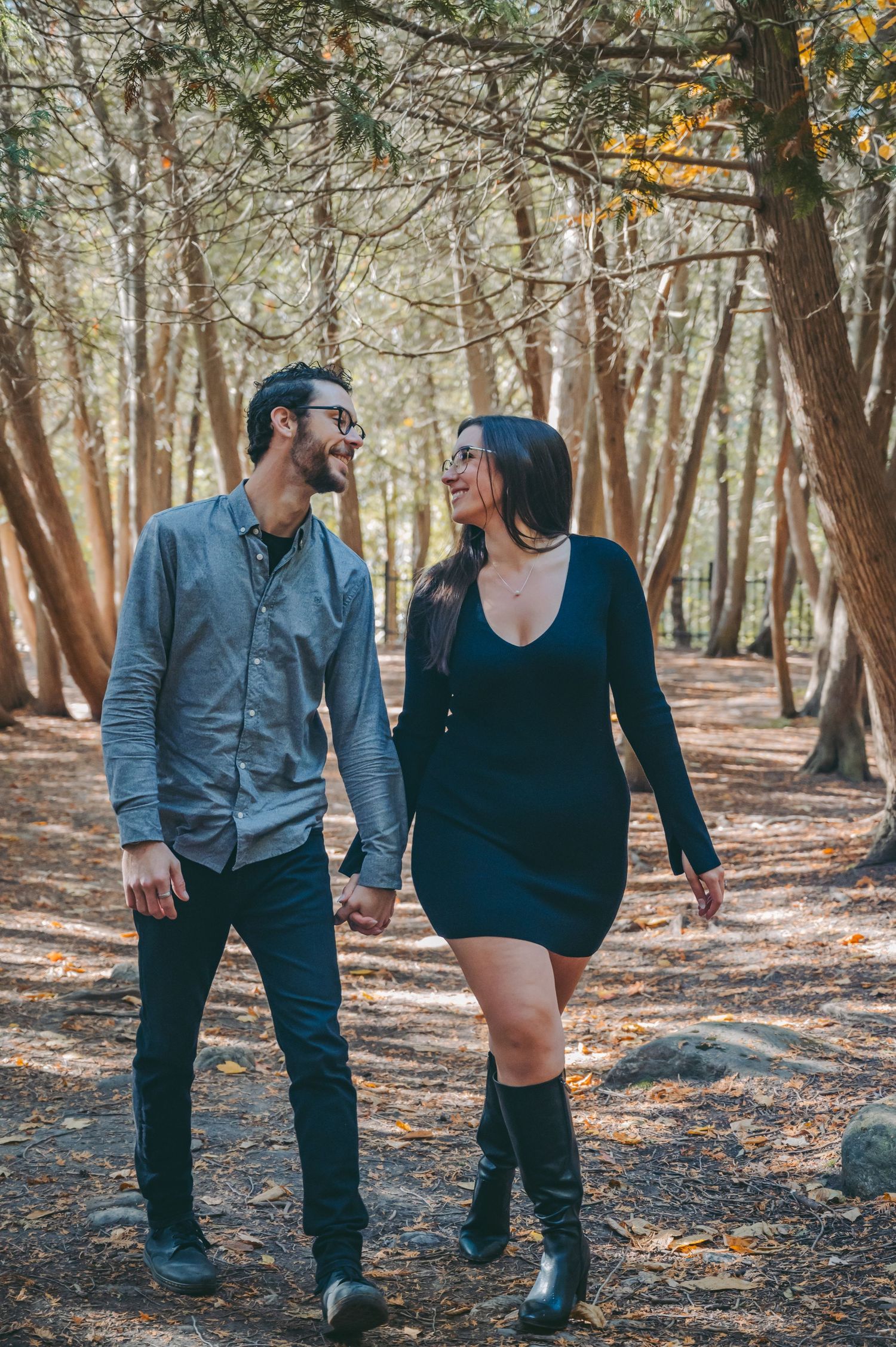 A stylish couple walking together on a forest trail lined with tall trees.