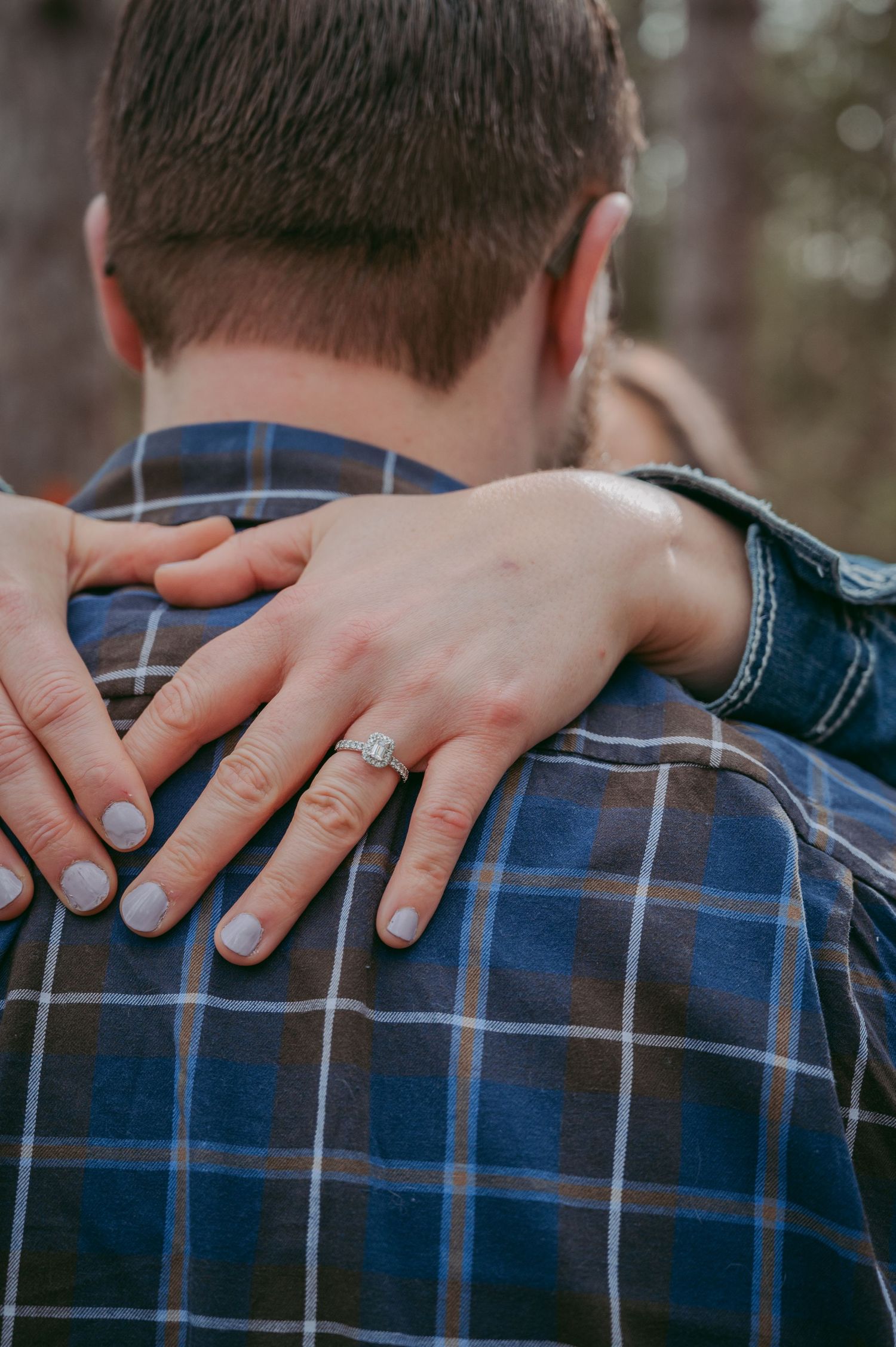 Close-up of hands wearing rings embracing against a plaid shirt backdrop.