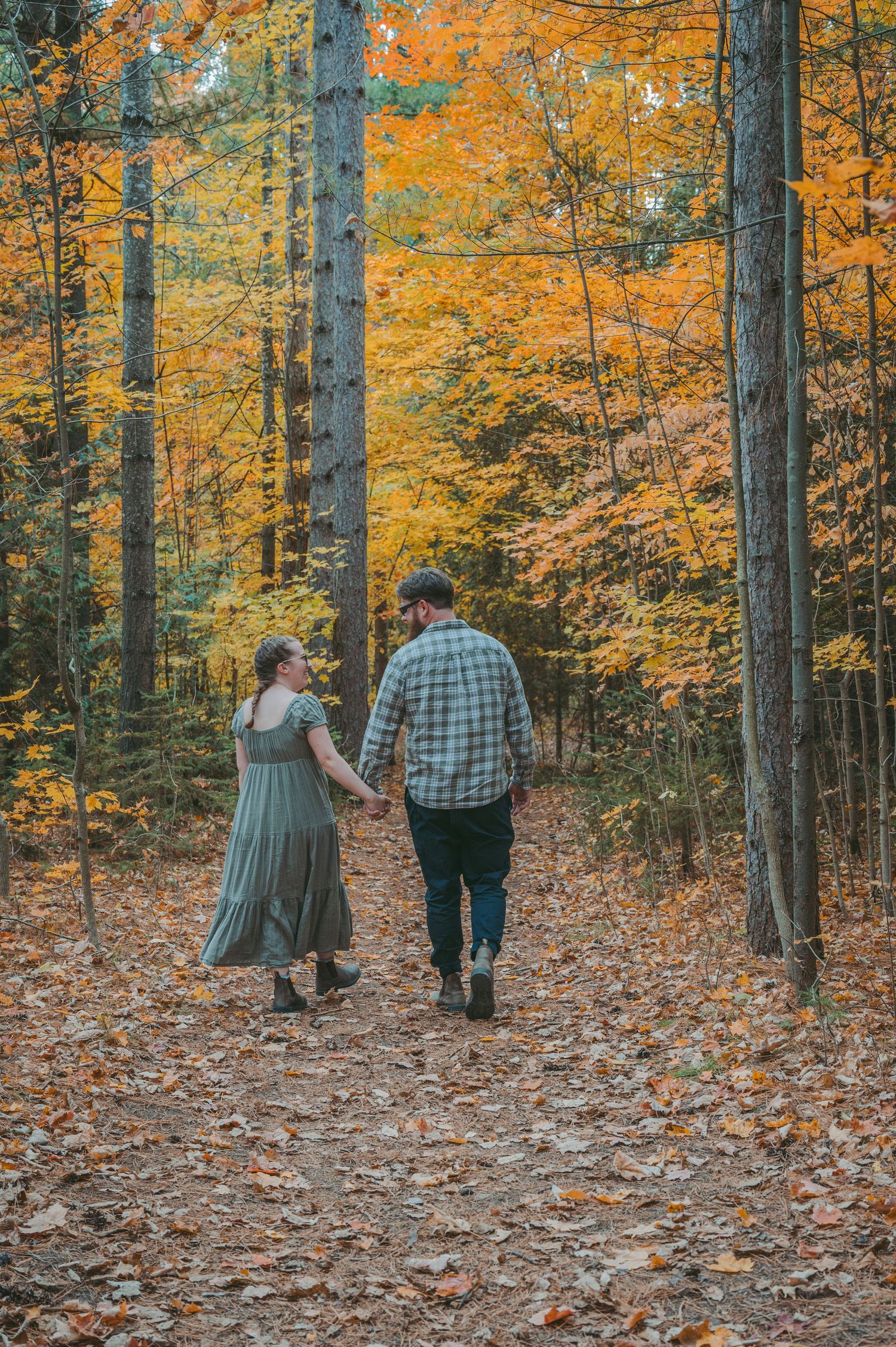 Couple walking hand in hand through vibrant fall forest with golden leaves.