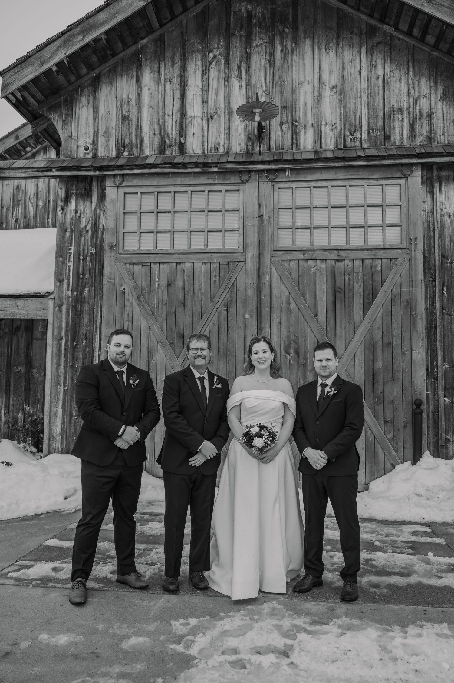 Bride and groomsmen pose in front of rustic barn doors in winter wedding photo.