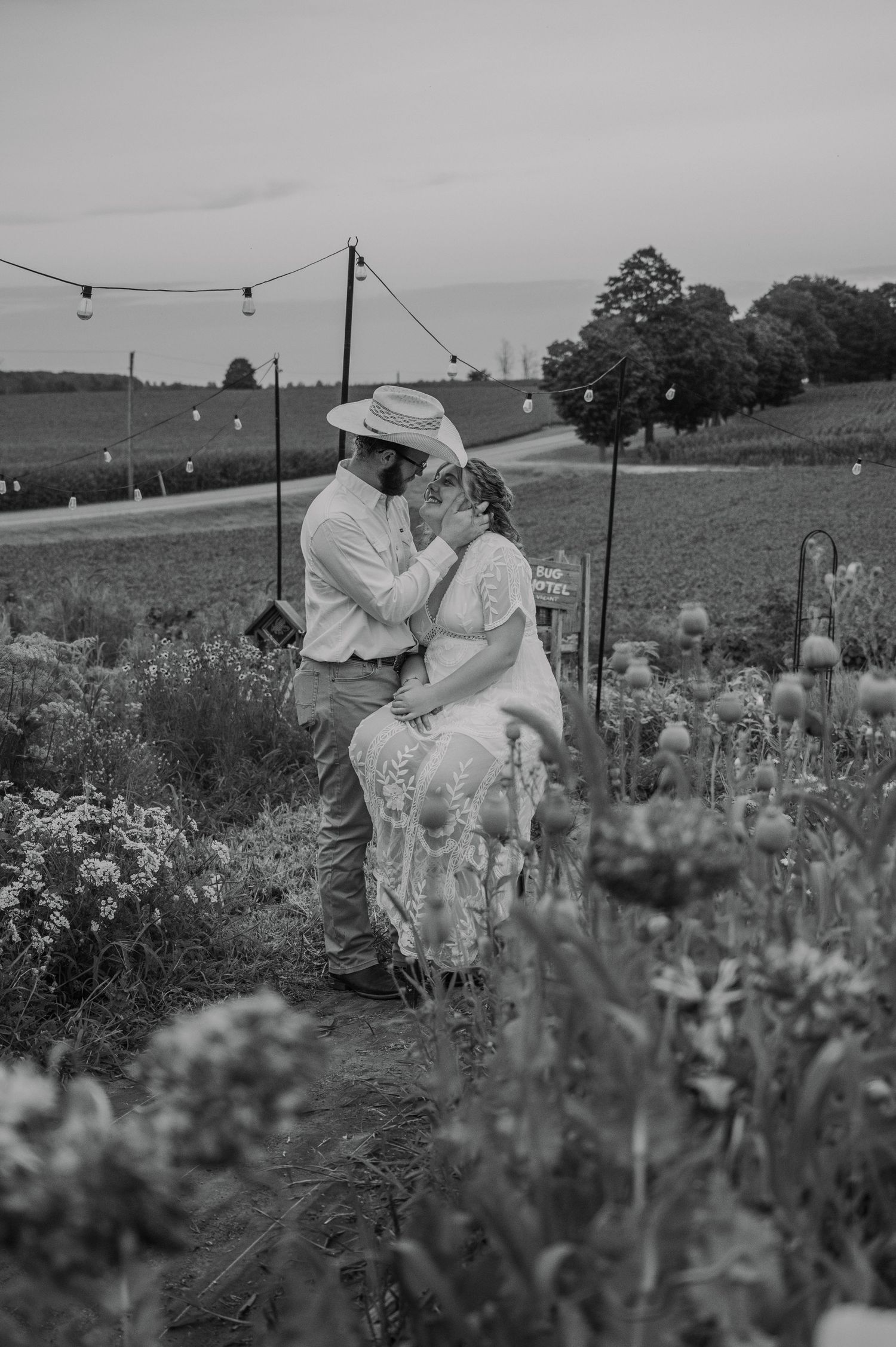 Black and white photo of a couple sharing a romantic moment in a flower field at a rustic outdoor wedding.