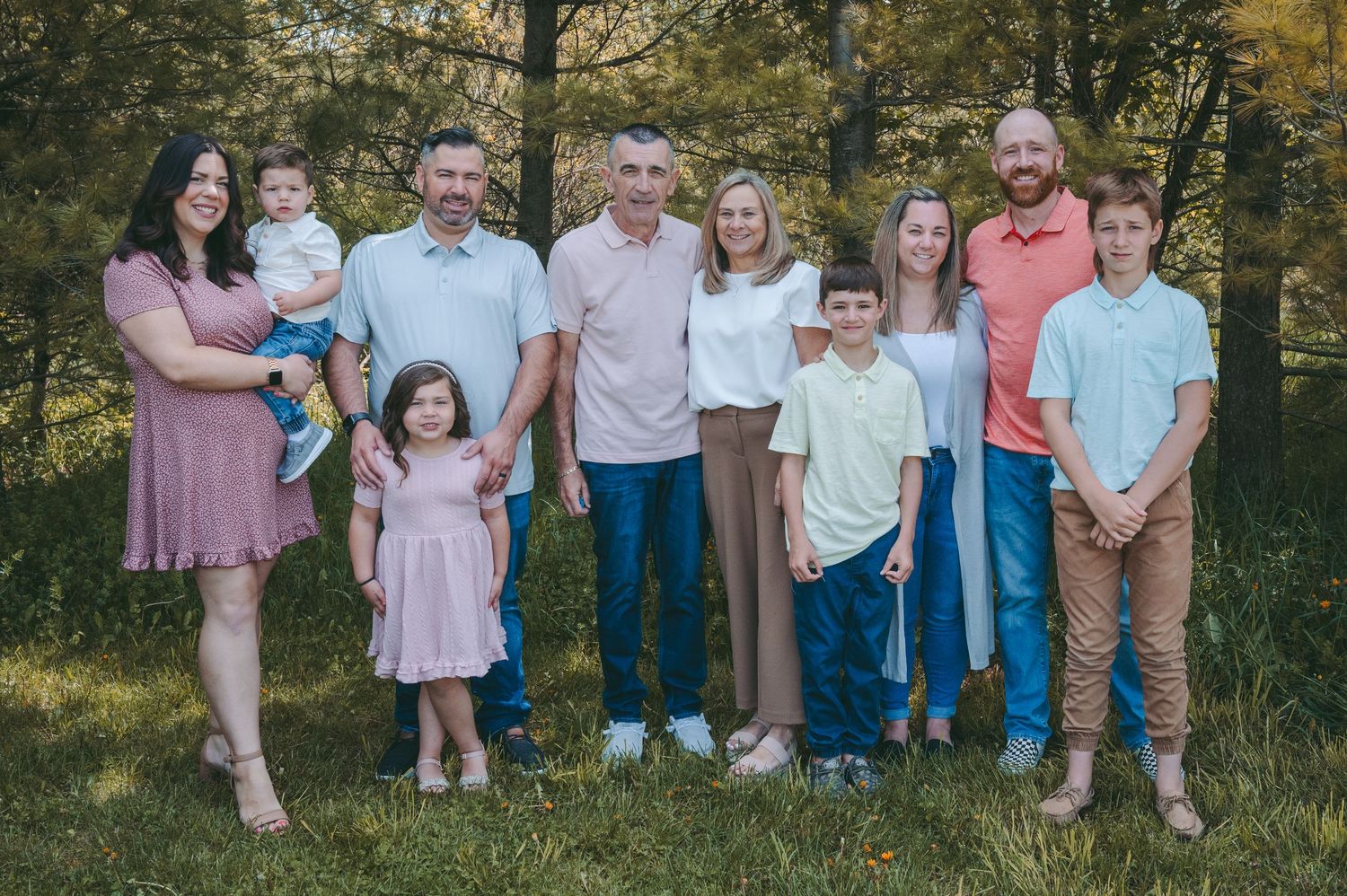 Large family group portrait outdoors with multiple generations in casual attire.