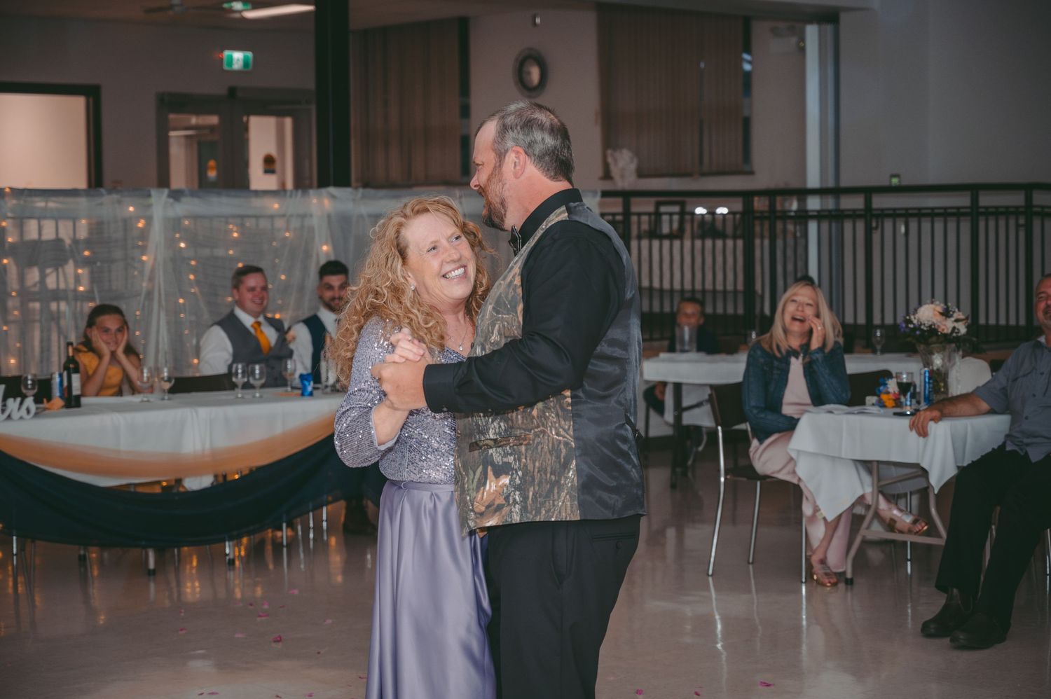 Couple dances together at wedding reception while guests look on from decorated tables.